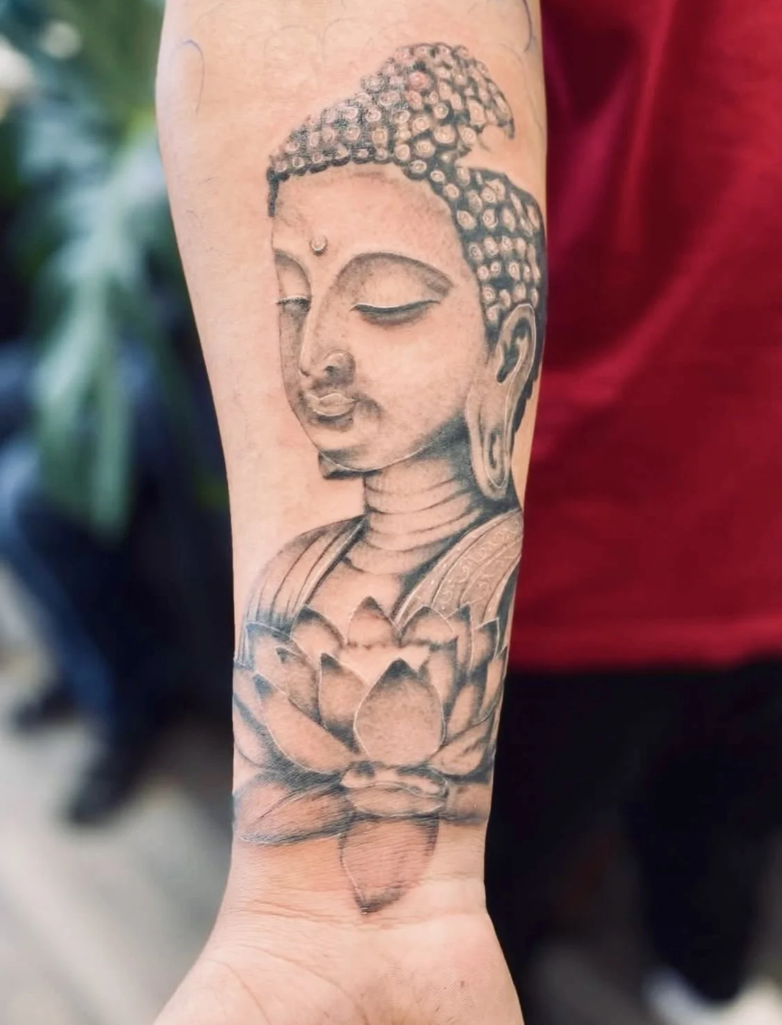 Tattoo of a serene Buddha's face with closed eyes above a lotus flower on forearm.