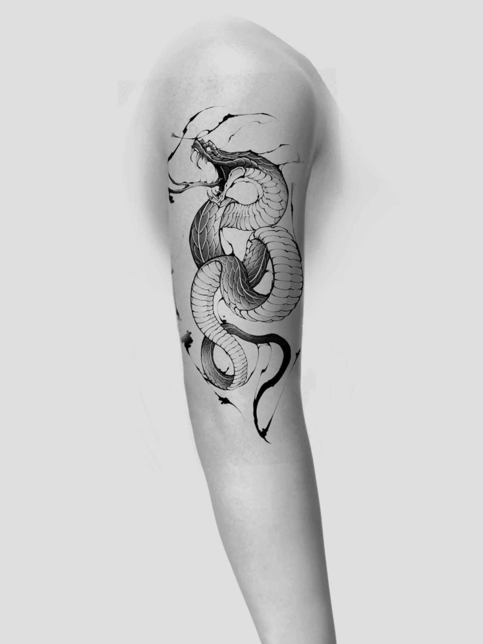Black and gray tattoo of a dragon on a person's upper arm, showing the dragon in a coiled position with its head raised and mouth open.