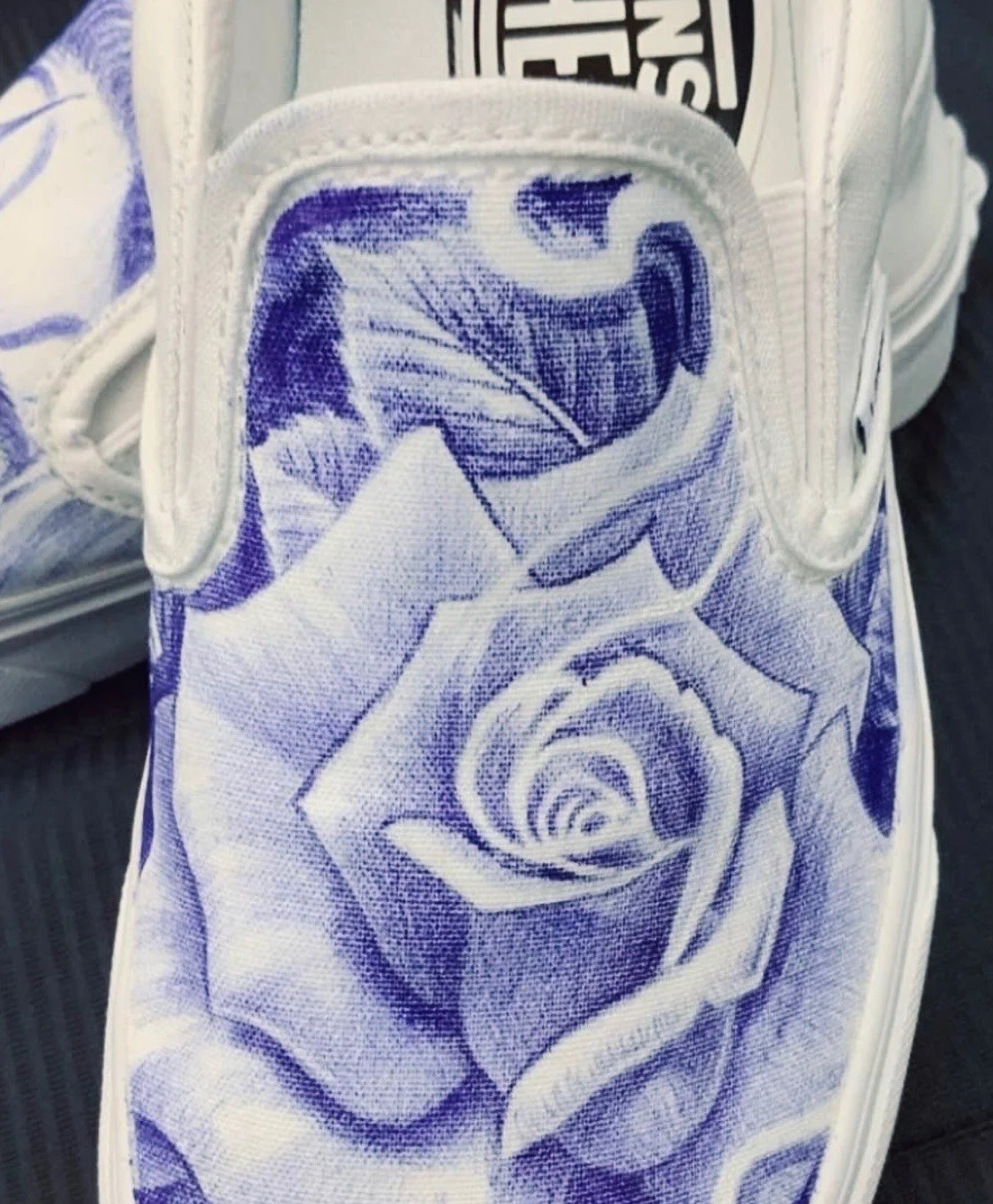 Close-up of a white sneaker with a blue floral and spiral pattern embroidered on the tongue.