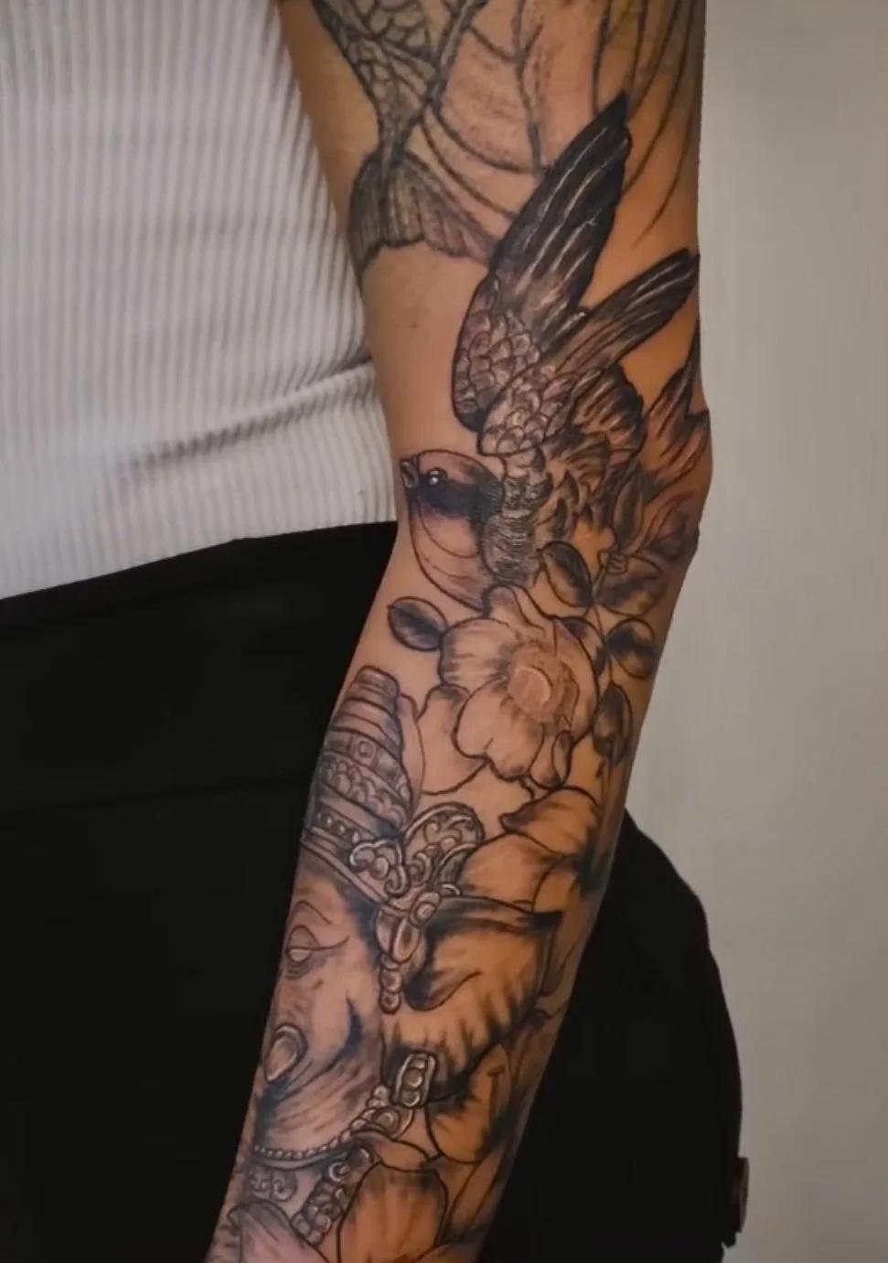 A detailed tattoo sleeve on a person's arm featuring a bird, flower, butterfly, and various decorative elements.