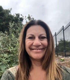 Debbie Freeman outdoors with greenery and a black metal fence in the background.