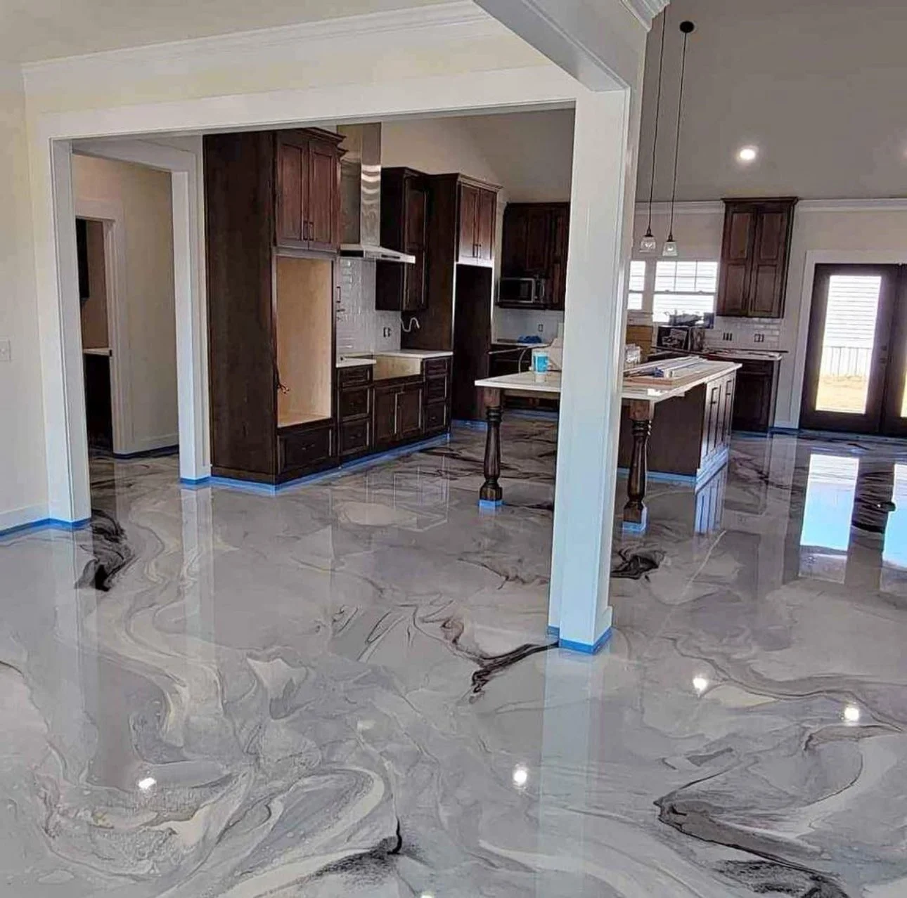 Spacious kitchen with marble flooring and dark wood cabinets, large island, and multiple windows and doors letting in natural light.