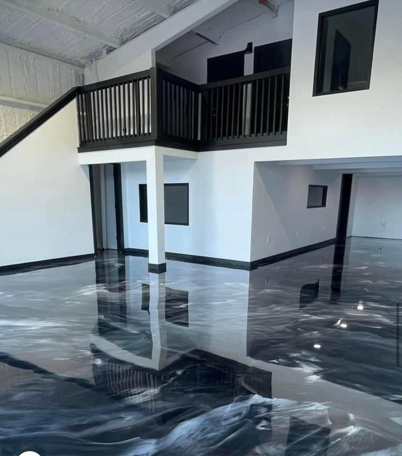 Interior of a building with black and white walls, black trim, and a black railing on a second-floor balcony, with a highly reflective black marble floor.