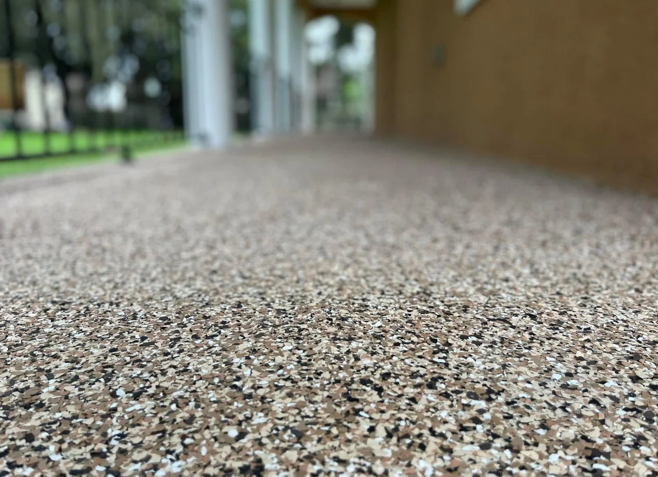 Close-up view of a speckled terrazzo floor with a blurred background of a porch and garden area.