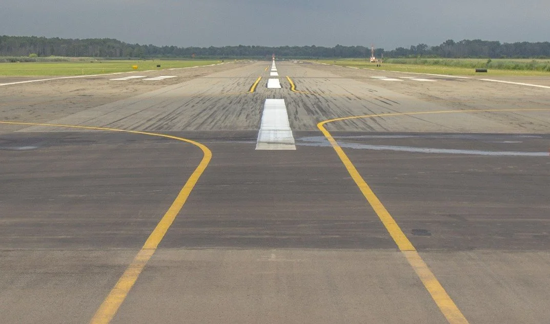 Runway at an airport with yellow taxi lines and a cloudy sky.