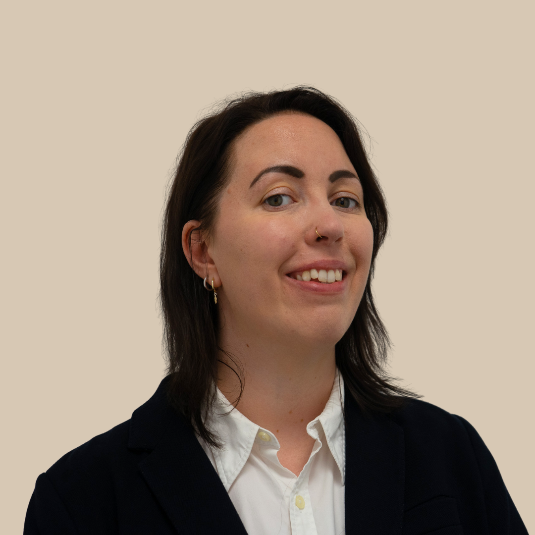 A woman with dark hair, wearing a white shirt and black blazer, smiling against a beige background.
