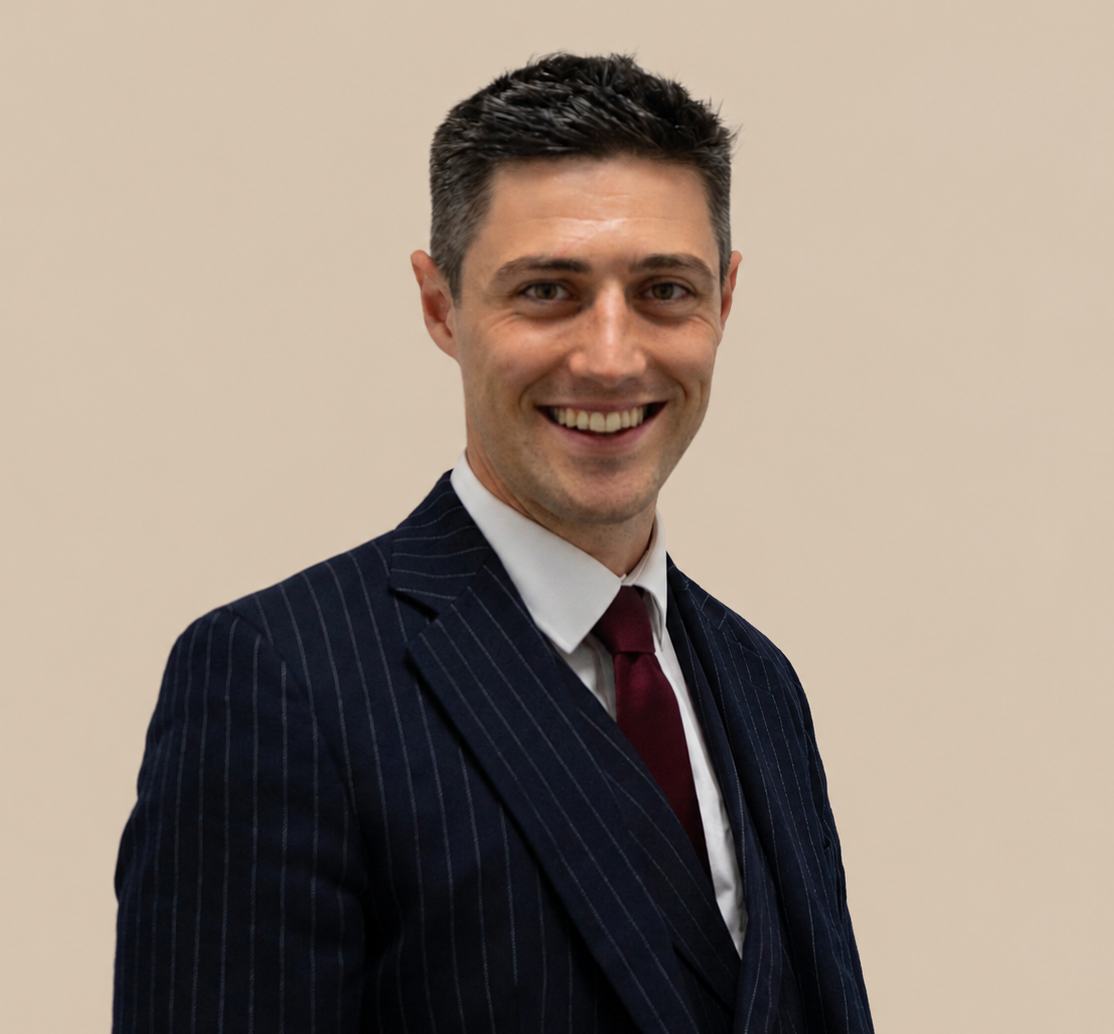 A smiling man in a dark pinstripe suit, white shirt, and maroon tie against a beige background.