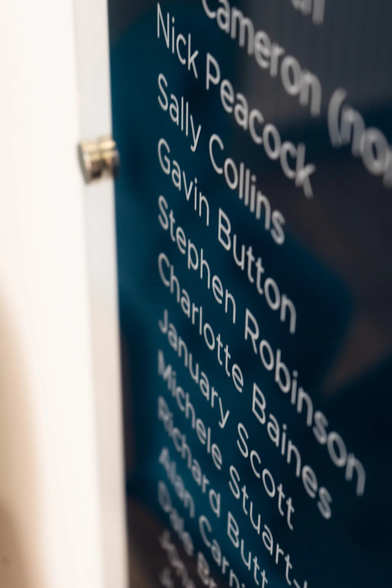 Close-up of a blue board with white text listing names of musicians or bands, including 'Nick Peacoak,' 'Sally Collins,' and 'Gavin Buton.'