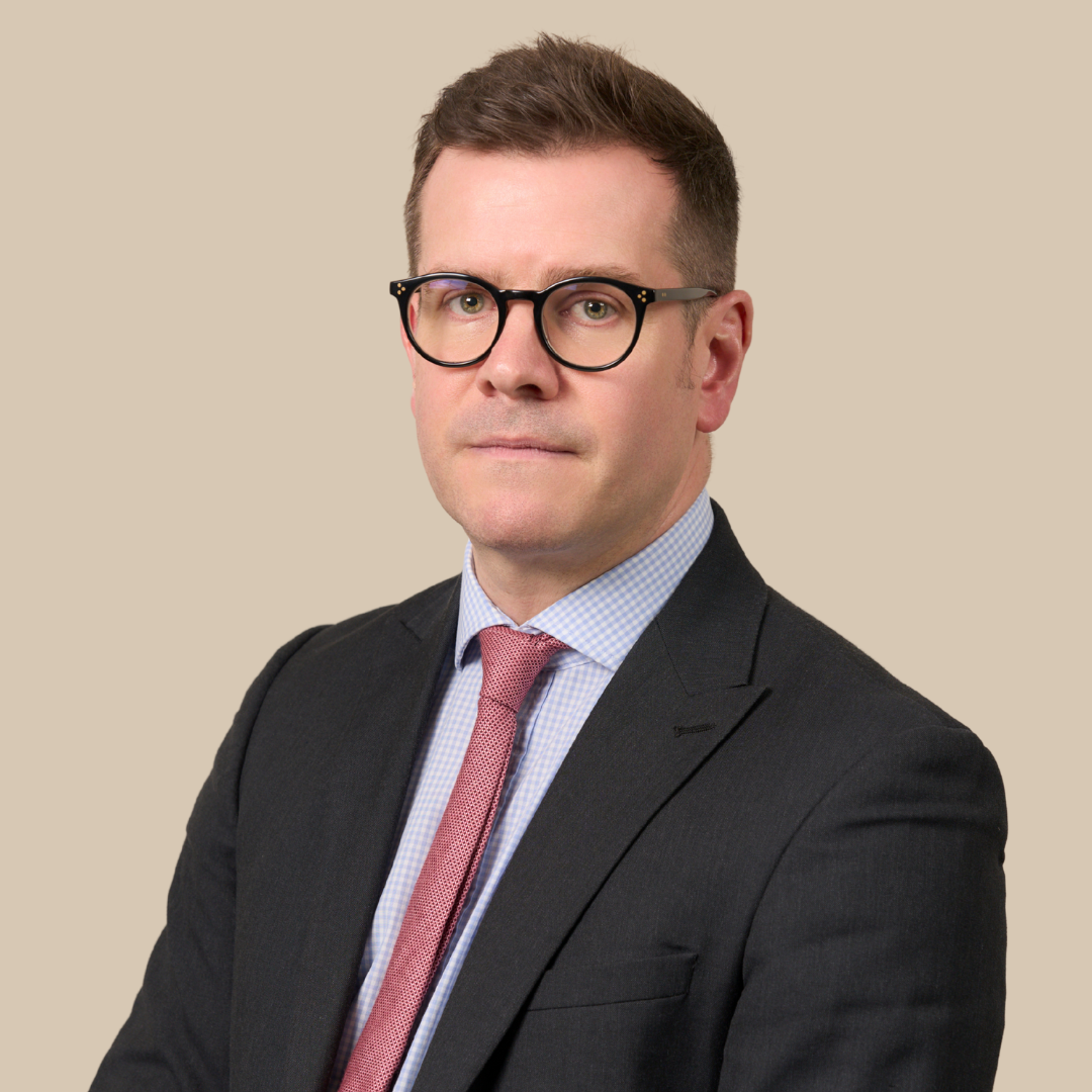 A professional man in a suit and glasses posing against a plain beige background.