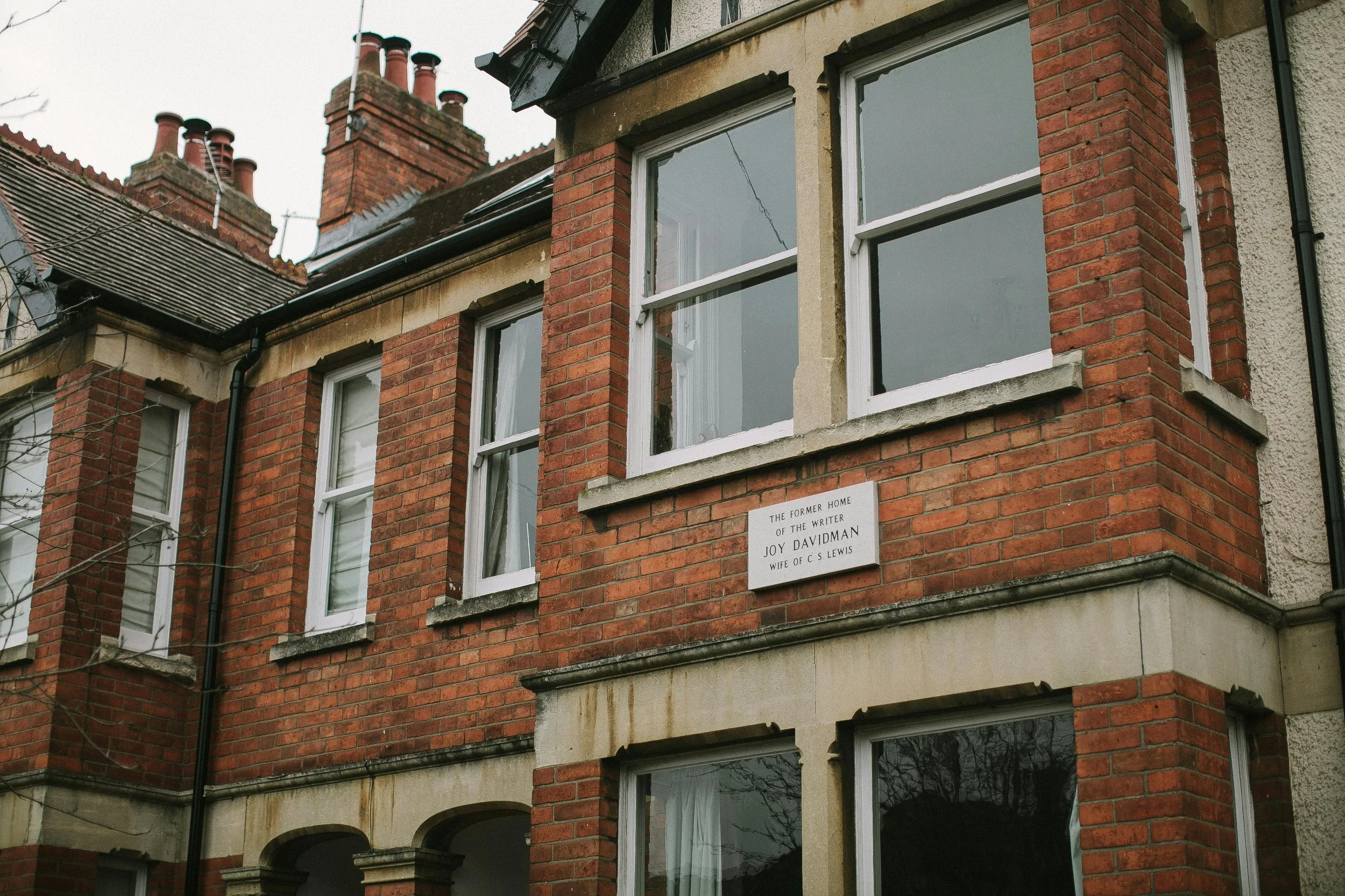Brick apartment building with white window frames and a commemorative plaque that reads, "The former home of the writer Joy Davidman, wife of C.S. Lewis."