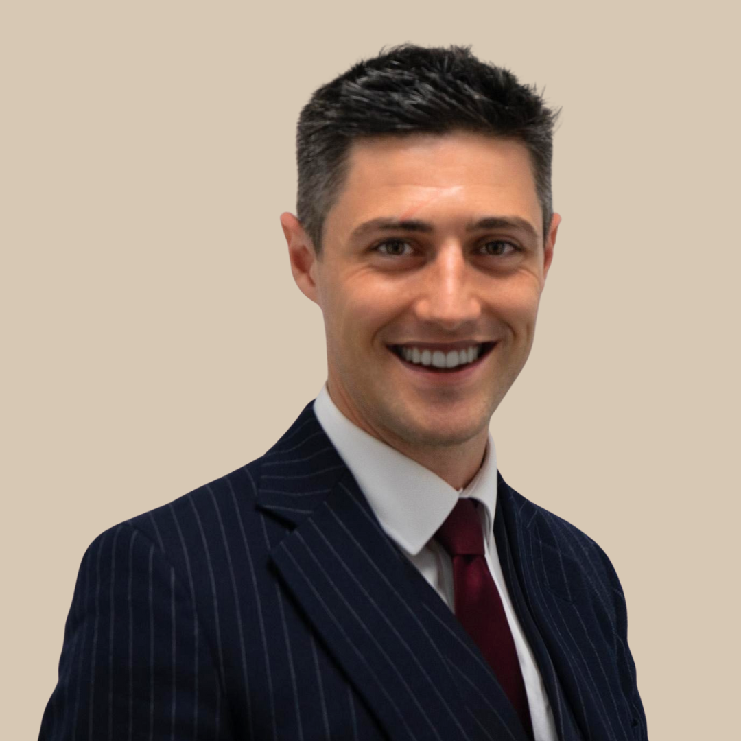 A smiling man in a dark pinstripe suit, white shirt, and burgundy tie, against a plain beige background.