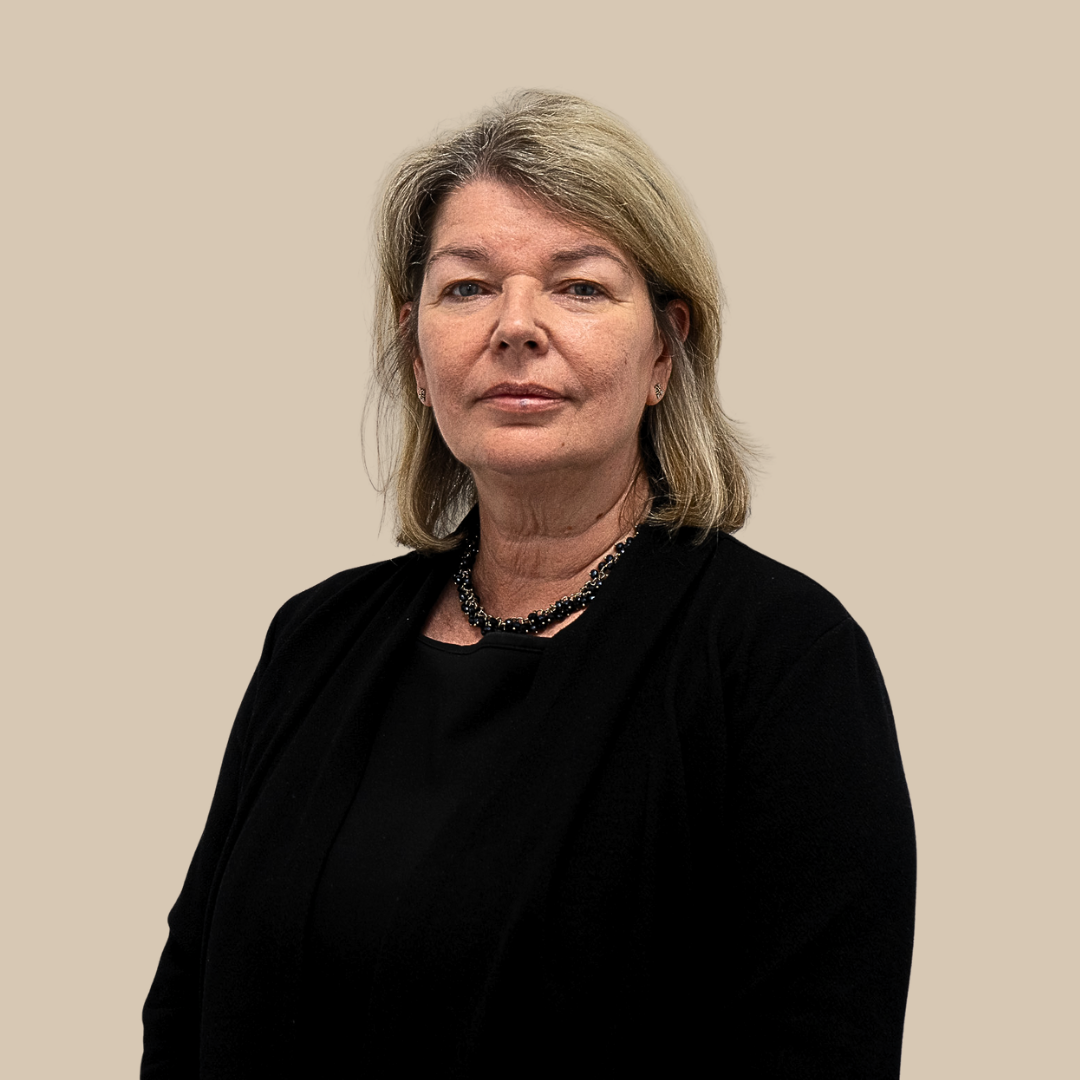 A professional woman with shoulder-length blonde hair wearing a black blazer and necklace, posing against a beige background.