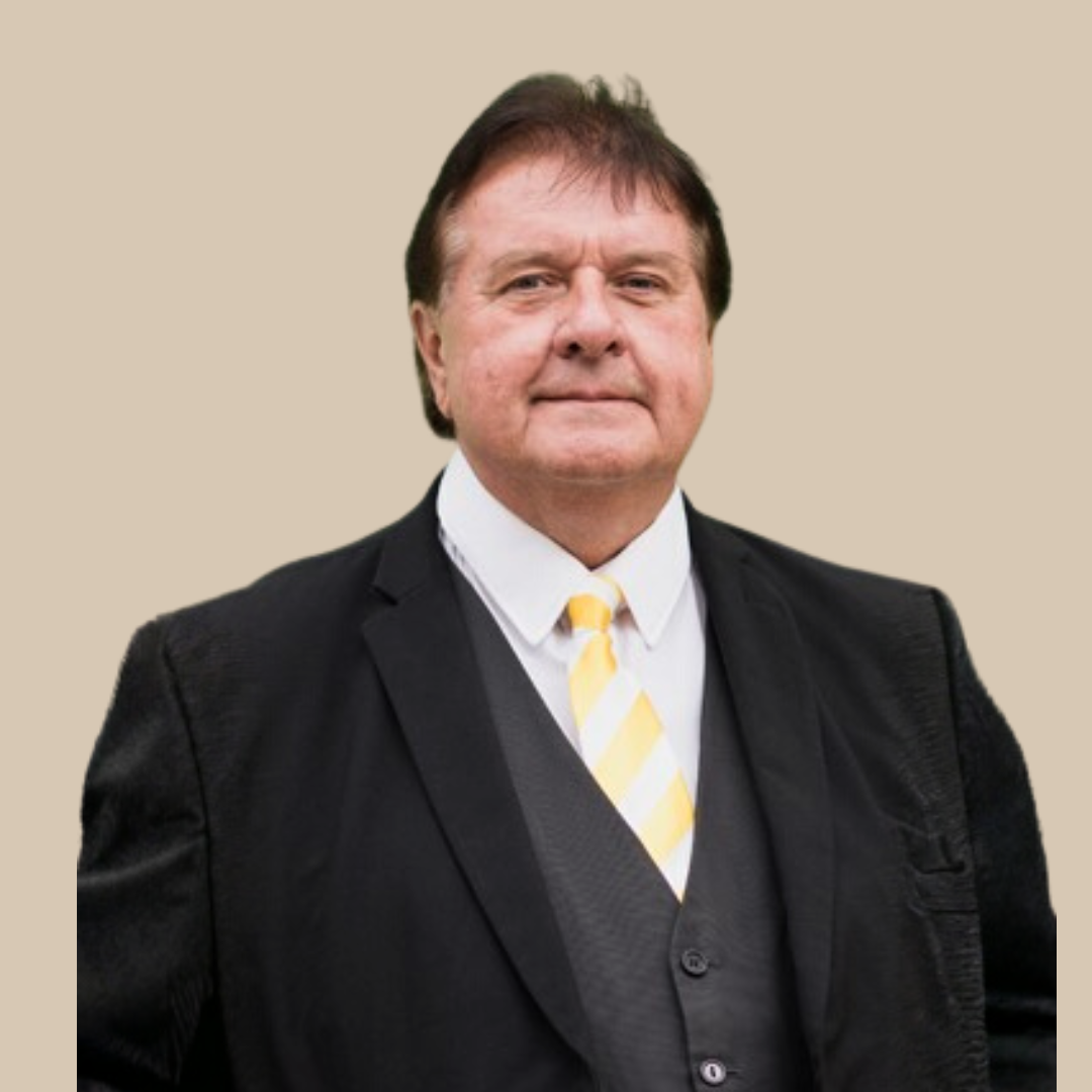 Portrait of a middle-aged man in a black suit, white shirt, and yellow-striped tie, standing against a beige background.