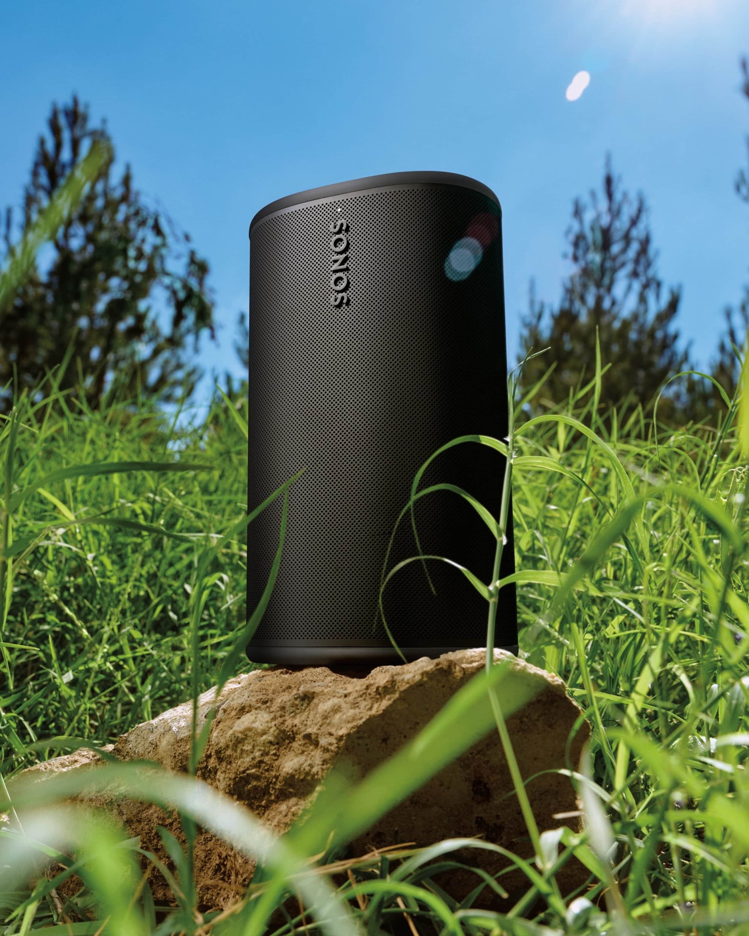 Sonos play portable speaker sitting outside on a rock surrounded by grass