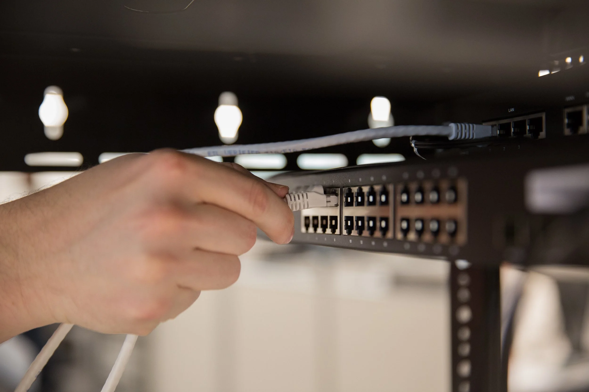 A hand plugs an Ethernet cable into a network switch in a server room.