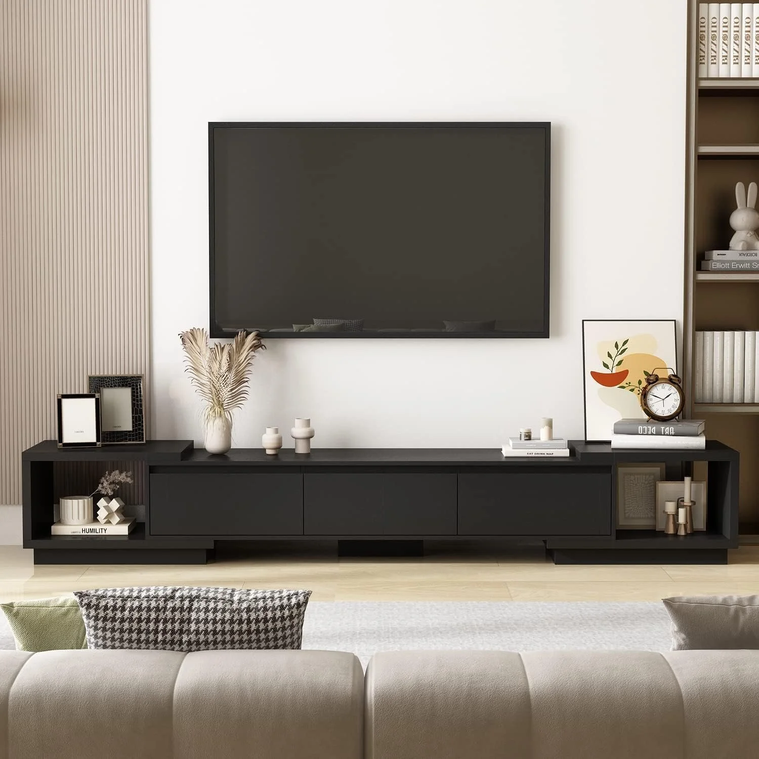 A modern living room with a wall-mounted TV, black TV stand, decor items, and a gray sofa in the foreground.
