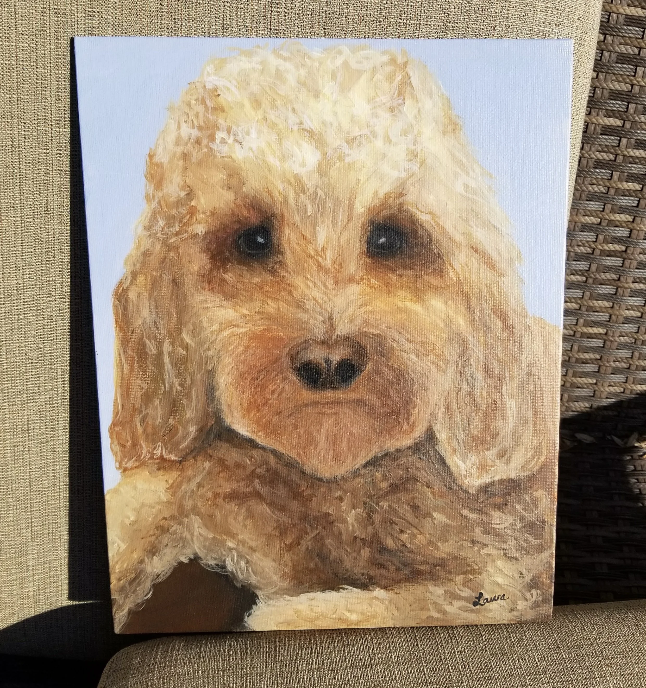 Painting of a dog with light brown and cream-colored fur, dark eyes, and a black nose, signed 'Laura' in the bottom right corner.