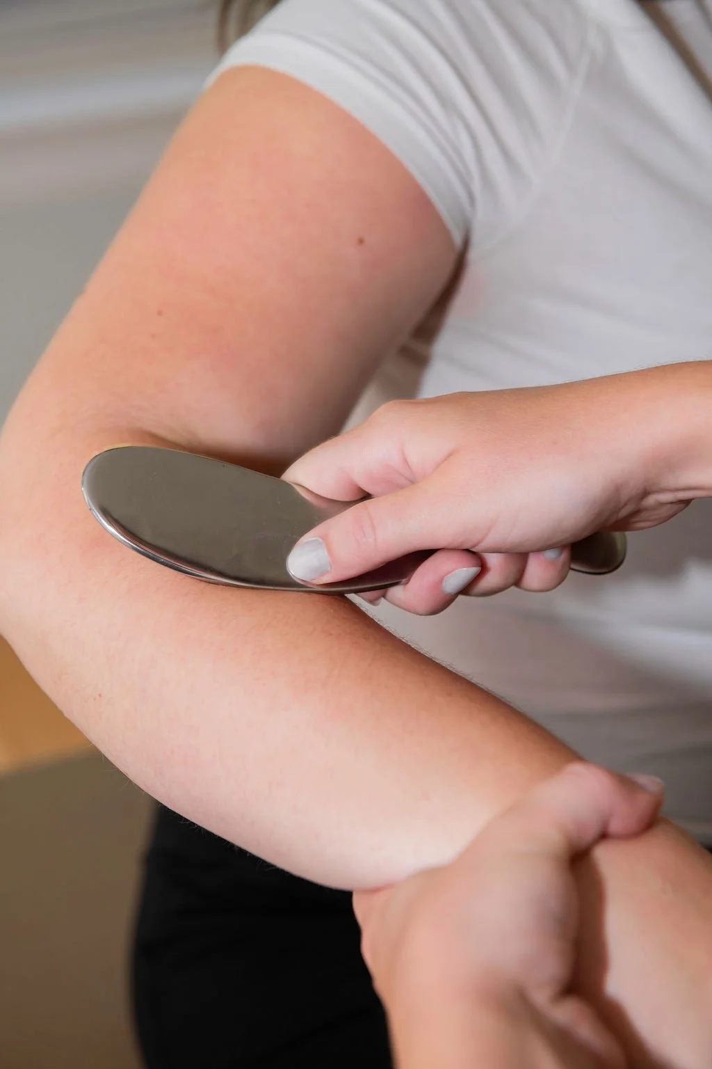 Person using a metal soft tissue therapy instrument on another person's forearm.