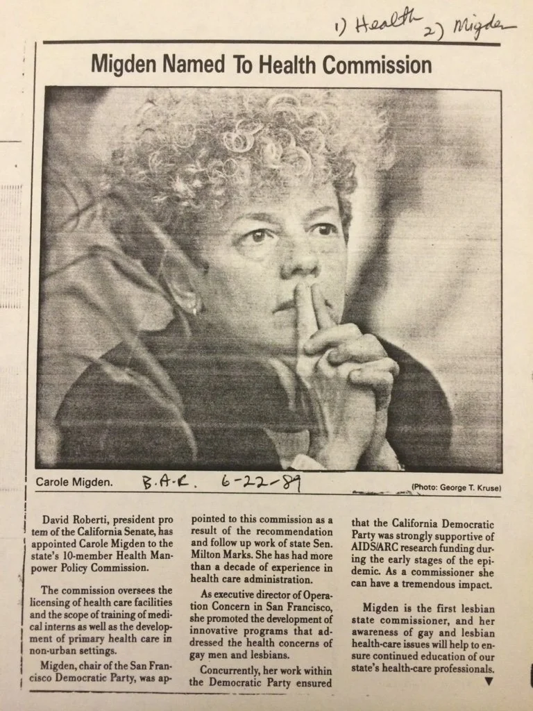 Black and white photo of a woman with curly hair, with her index finger touching her lips, sitting in front of a newspaper headline titled 'Migden Named To Health Commission'.