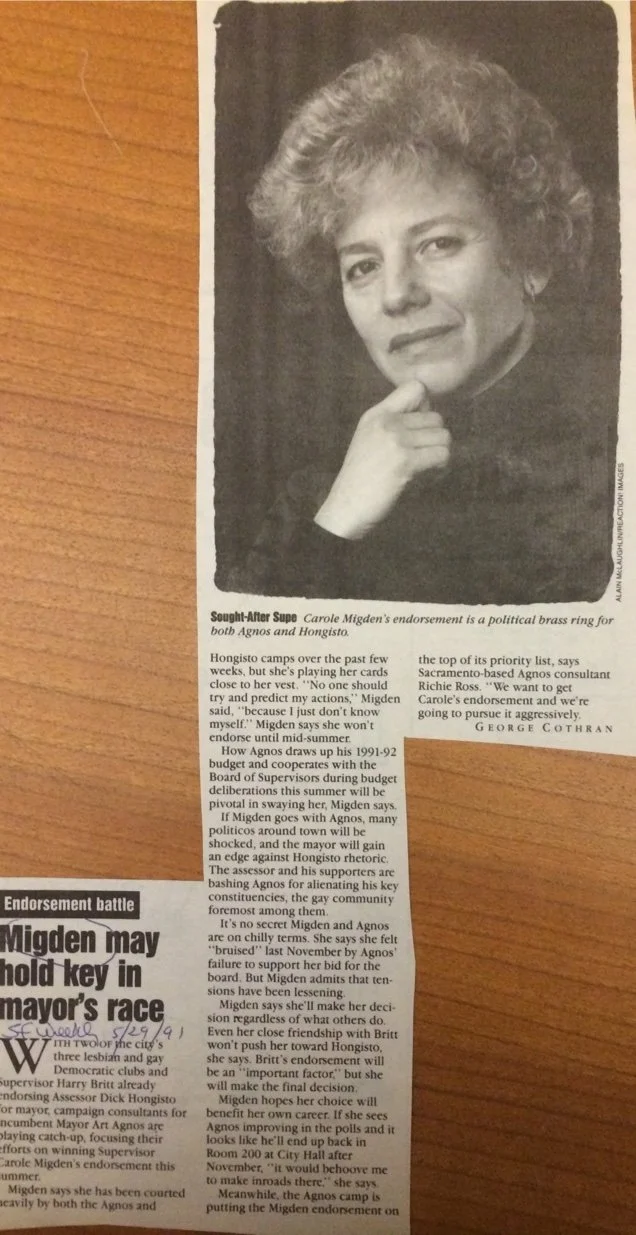 Black and white photo of a woman with curly hair, resting her chin on her hand, looking into the camera.