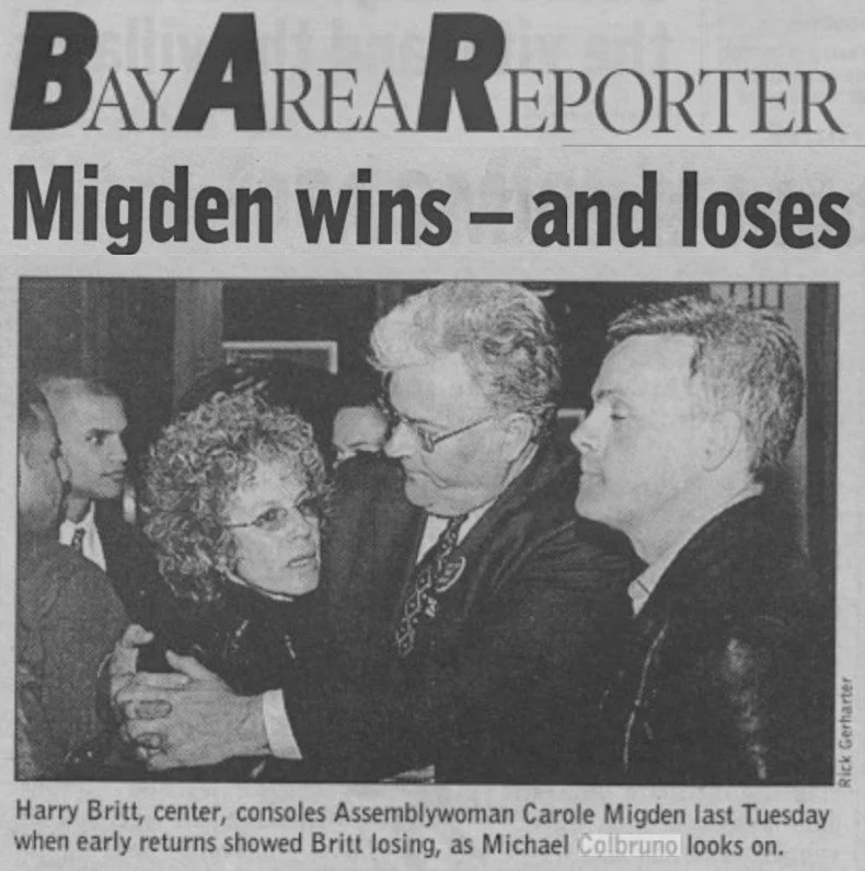 Black and white newspaper photo showing Harry Britty, center, consoling Assemblywoman Carole Migden. Migden, appearing upset, is being held by Britty. A man with glasses and another man with a mohawk hairstyle are observing them.