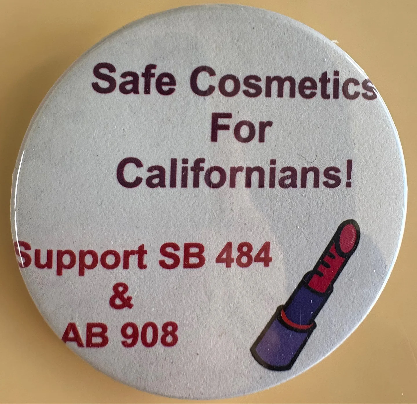A button advocating for safe cosmetics for Californians, supporting bills SB 484 and AB 908, with an illustration of lipstick.
