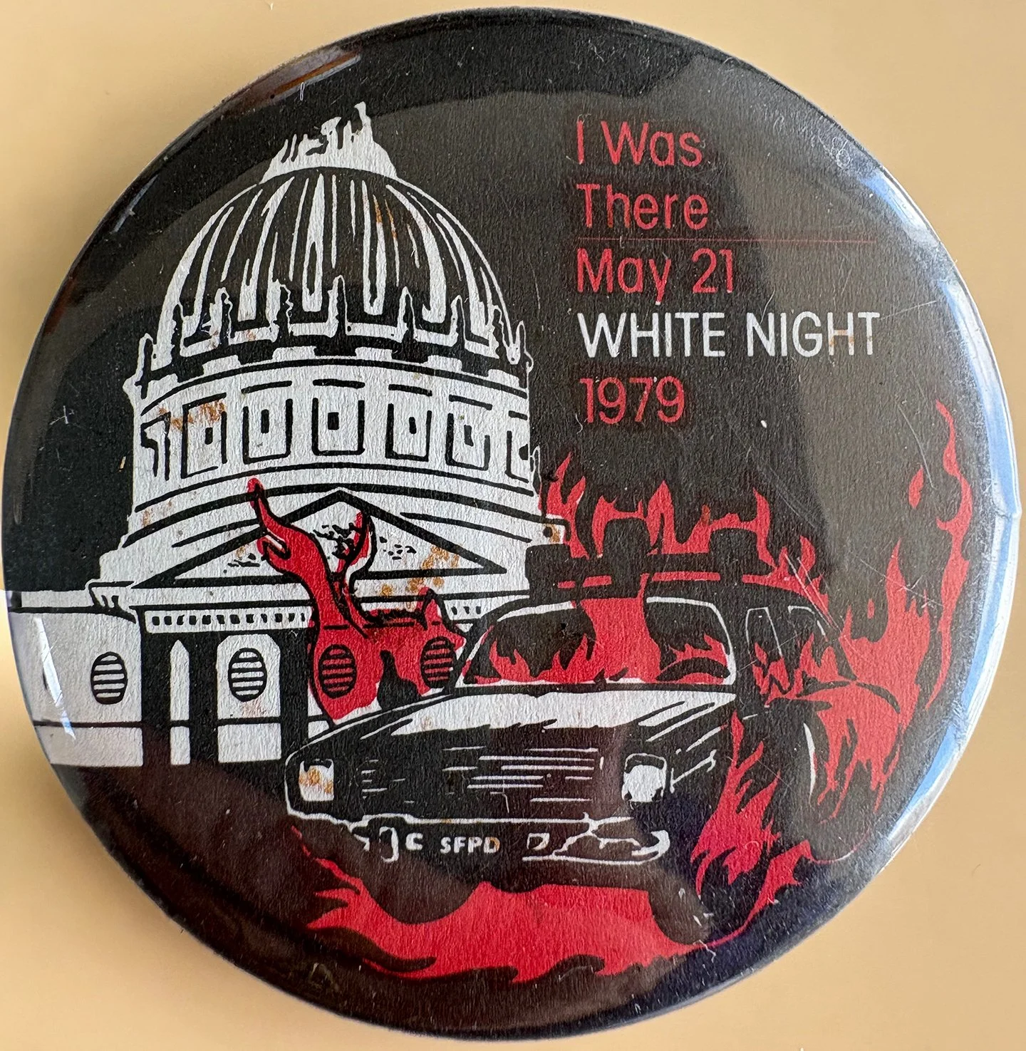 A pin-back button with a black background featuring an illustration of the U.S. Capitol building, a police car labeled 'SFPD,' a flaming object, and red fire with the text 'I Was There May 21, 1979, WHITE NIGHT'.