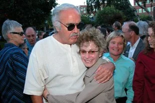 Senator John Burton hugging Carole Migden with her wife Cris looking on.