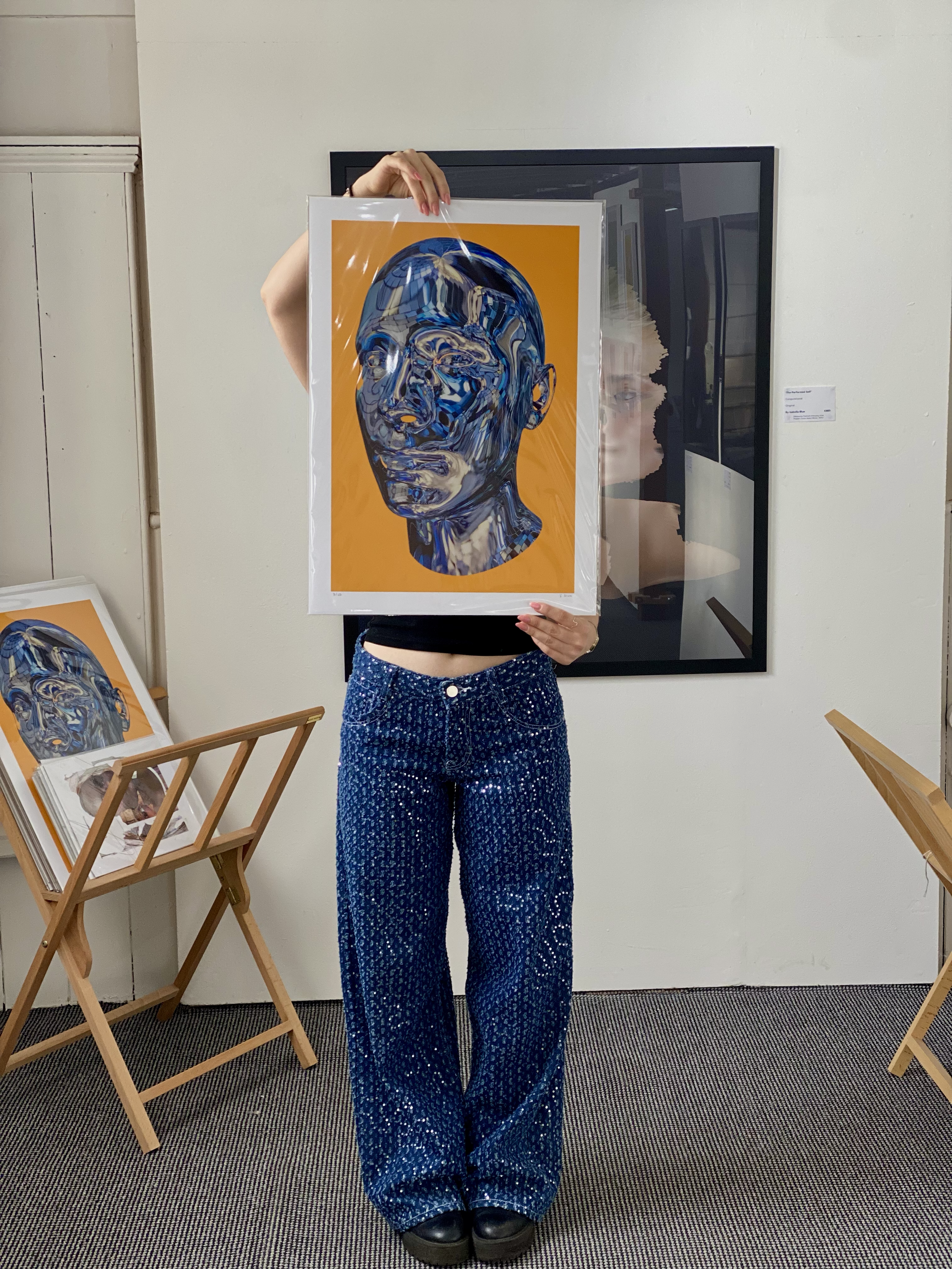 Person holding an art print of a male head made out of blue disco ball pieces on an orange background.