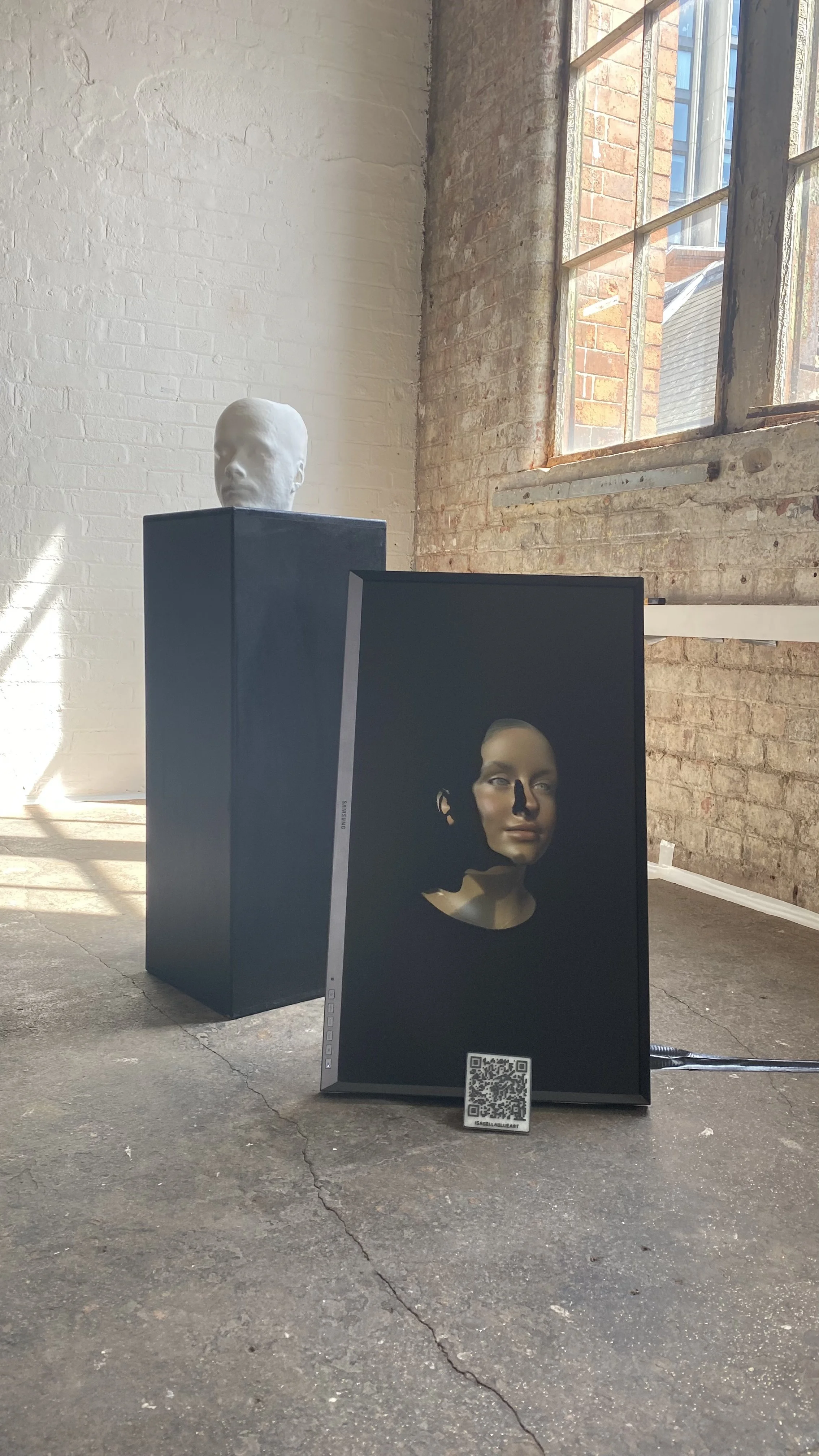 An art installation with a digital portrait of a woman's head displayed on a screen which sits on the floor inside an industrial room.