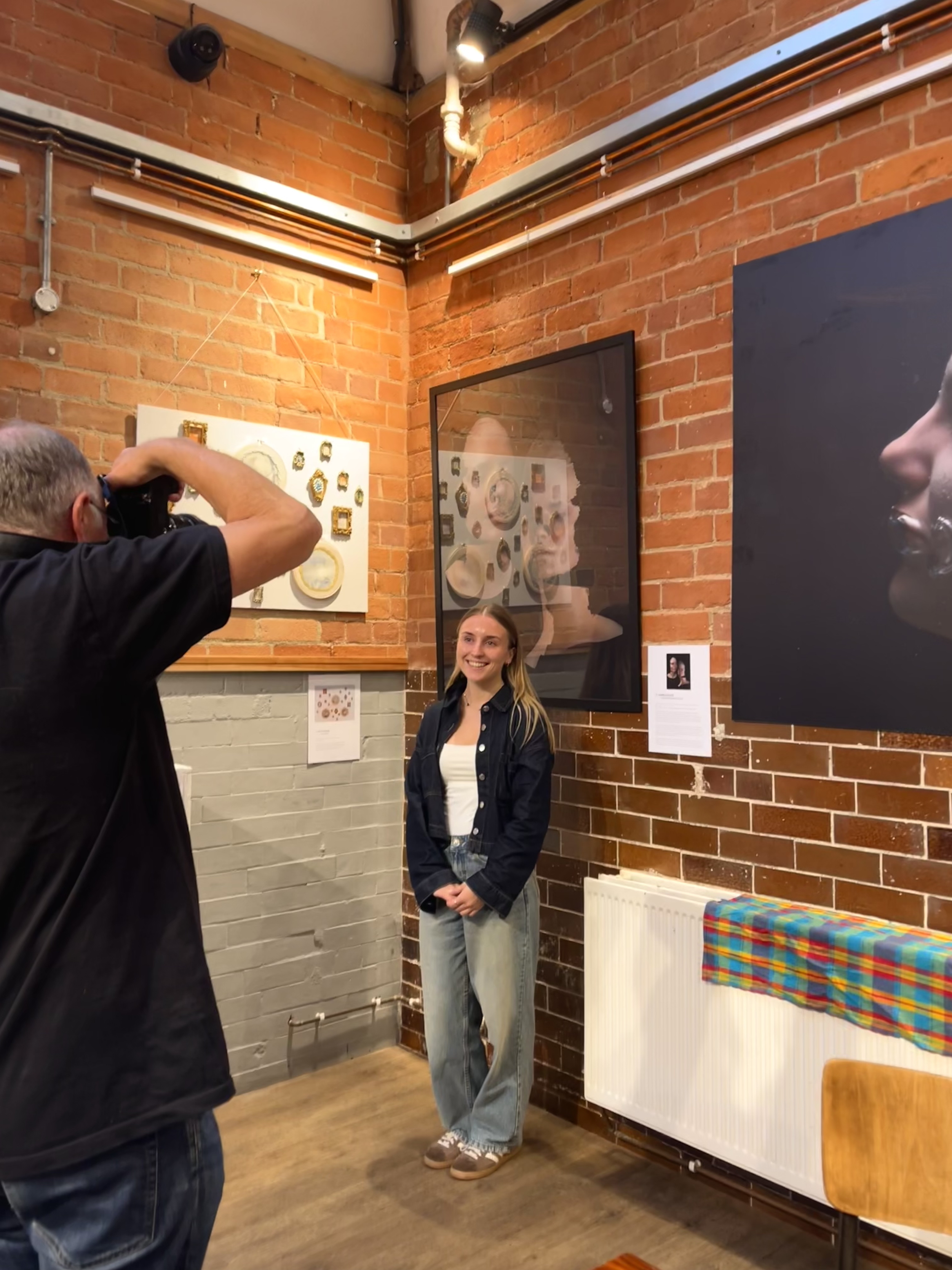 A woman in a navy jacket and jeans is smiling for a photo in an art gallery.