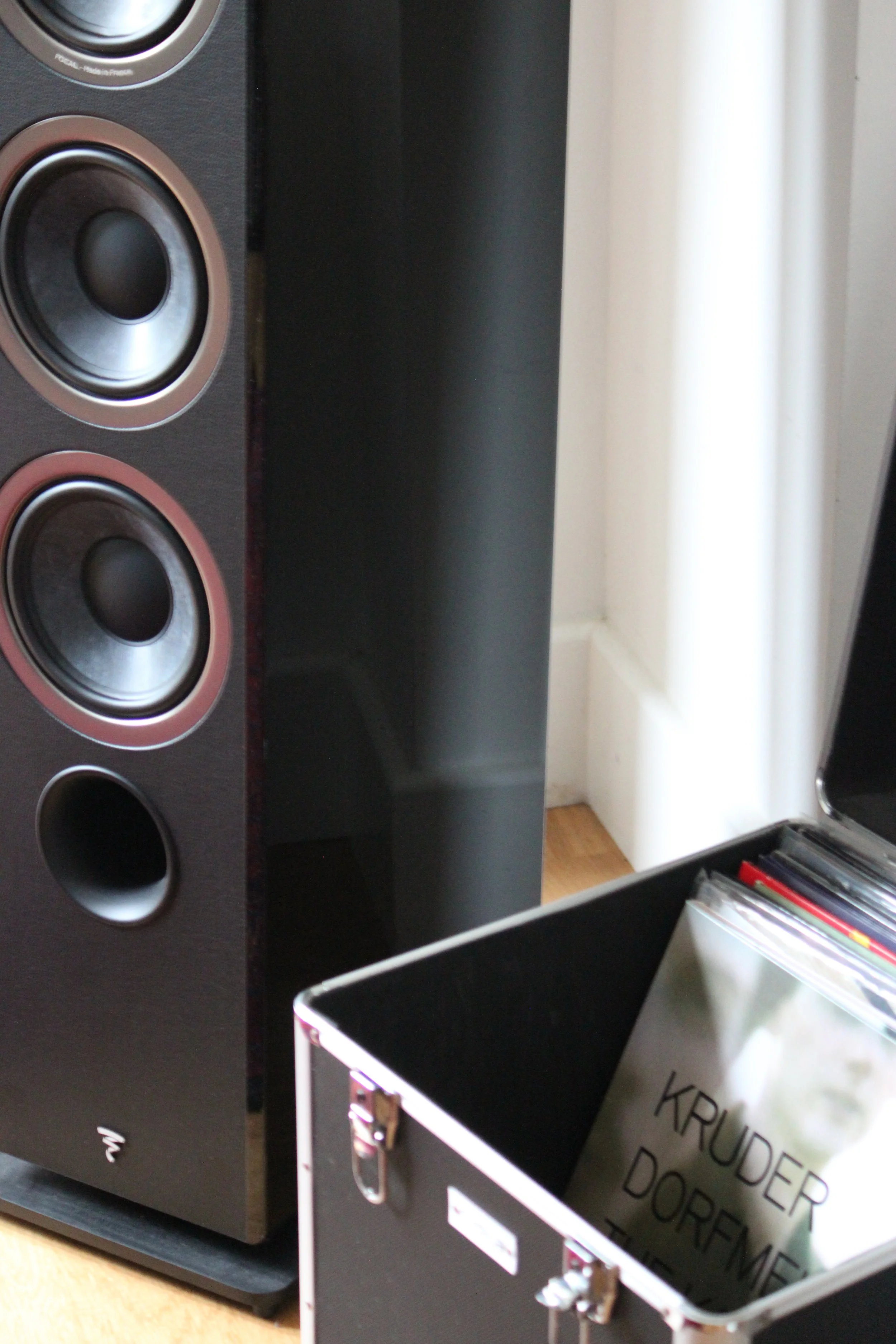A black speaker with a box of records beside it.