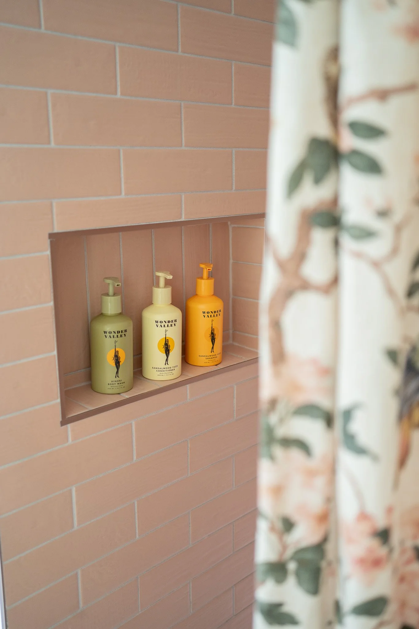 trio of wonder valley hair and body care products lay on self in pink tiled shower with floral curtain