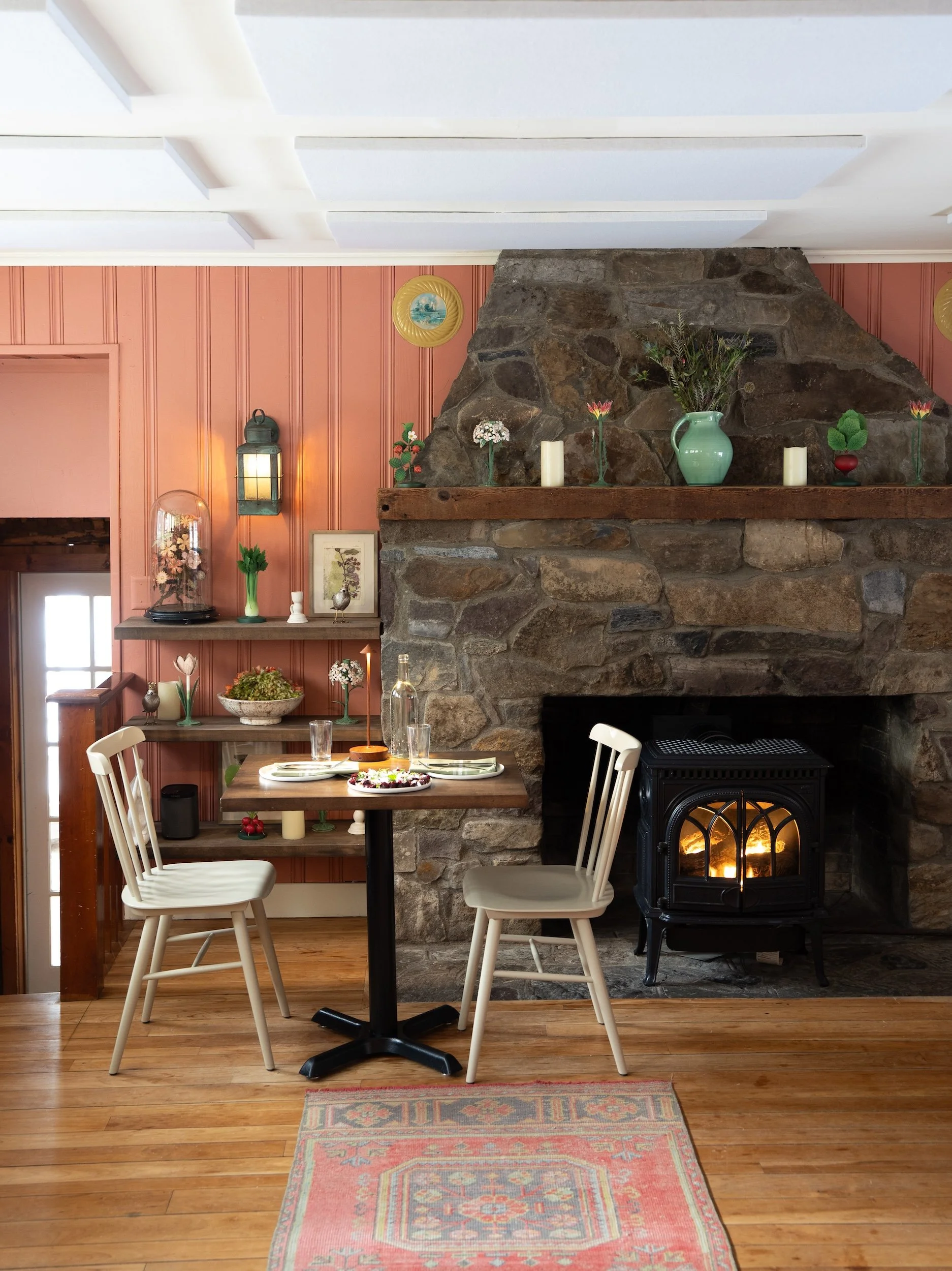 Bright clay colored walls, a cozy wood stove, and charming folk art decor in the library dining room at the Tillerman Inn & Restaurant.