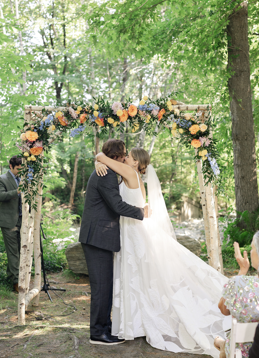 bride and groom kissing under a flower arch altar by the creek in the woods in Vermont