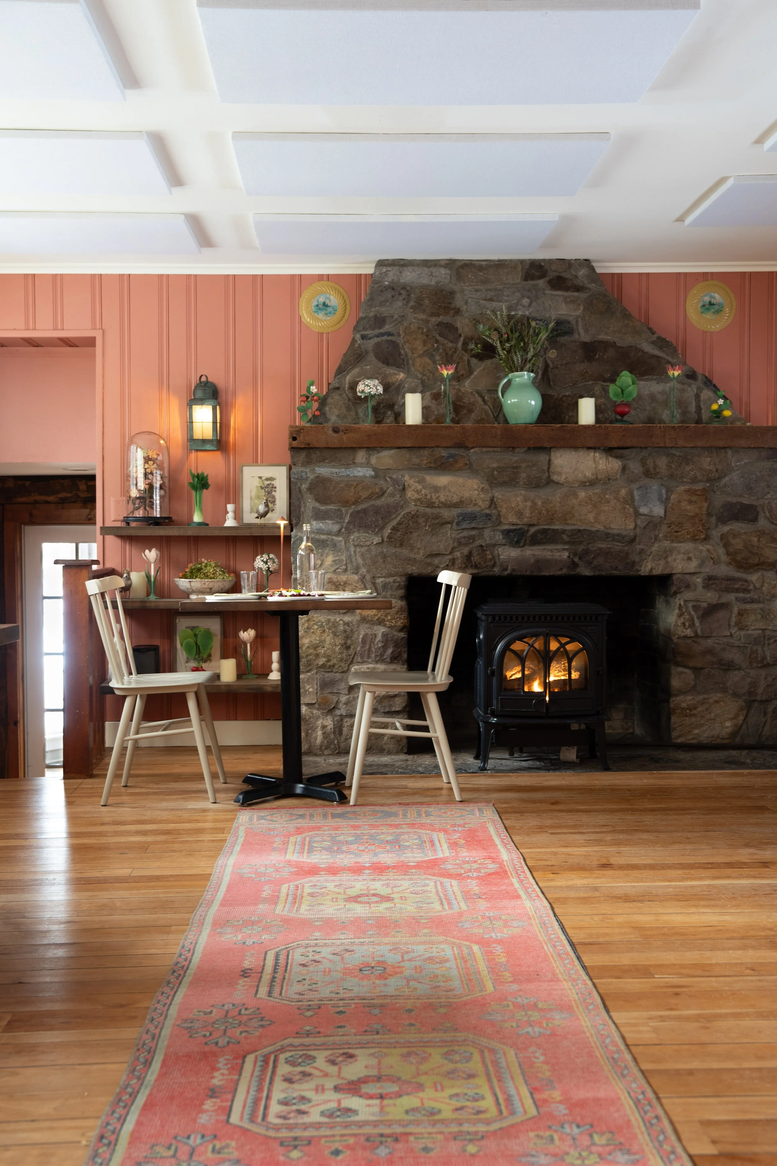 dinner in the library by the wood stove- a pink-ish clay colored dining room with a stone hearth and mantel decorated with whimsical folk art pieces. 