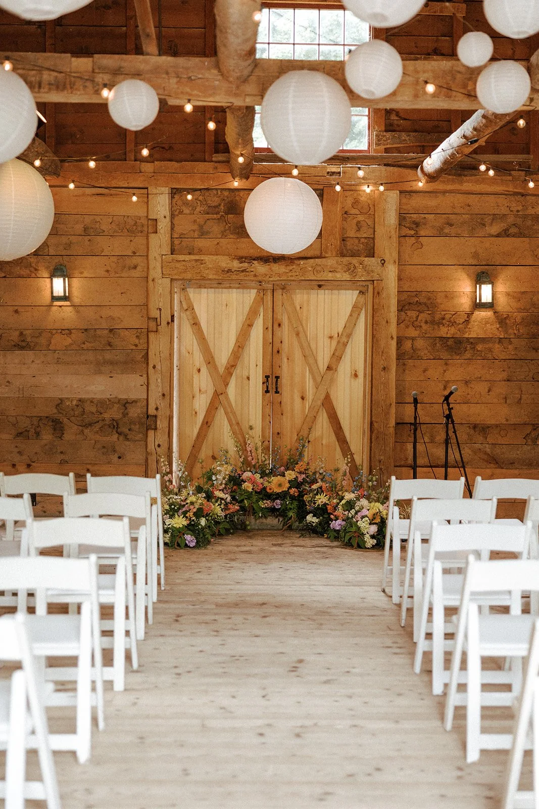 Our ceremony location inside the barn, with paper lanterns and beautiful florals at The Tillerman in Bristol, Vermont