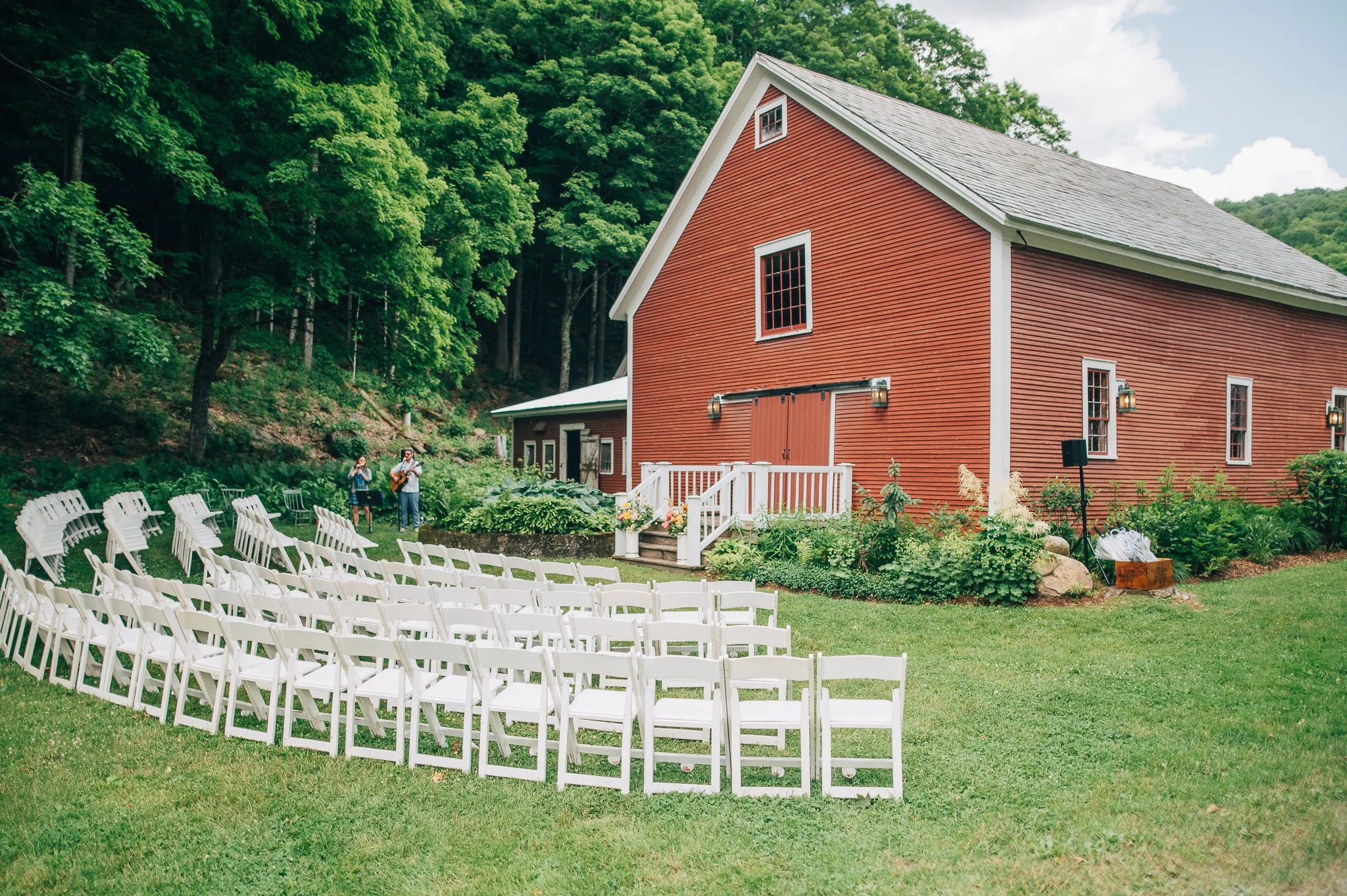 Outdoor wedding setup in front of the red barn in The Tillerman Inn in Bristol, VT with white chairs arranged for guests and floral decorations at the entrance