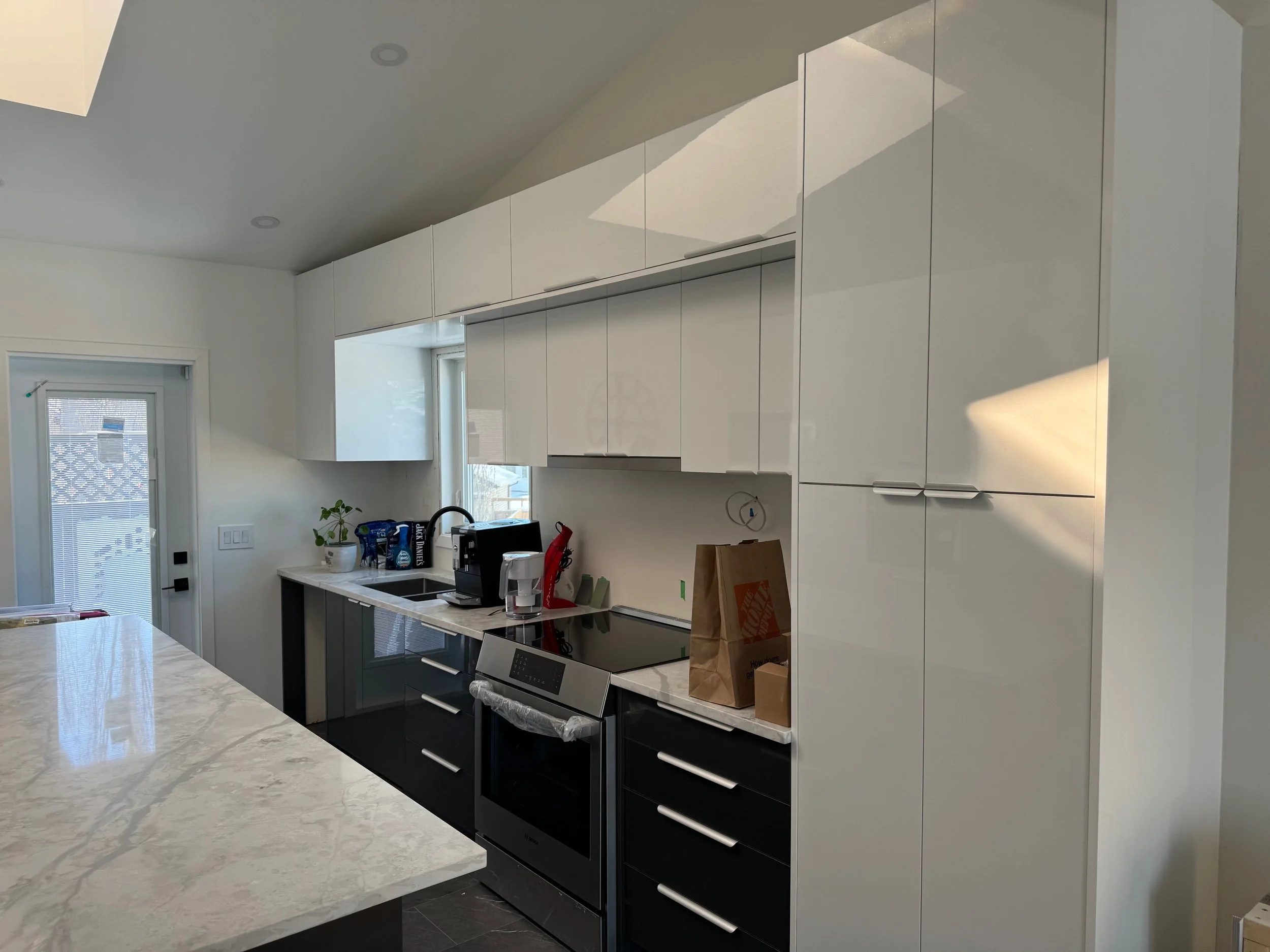 Modern kitchen with white cabinets, marble countertop island, black and stainless steel appliances, and small potted plant near window.