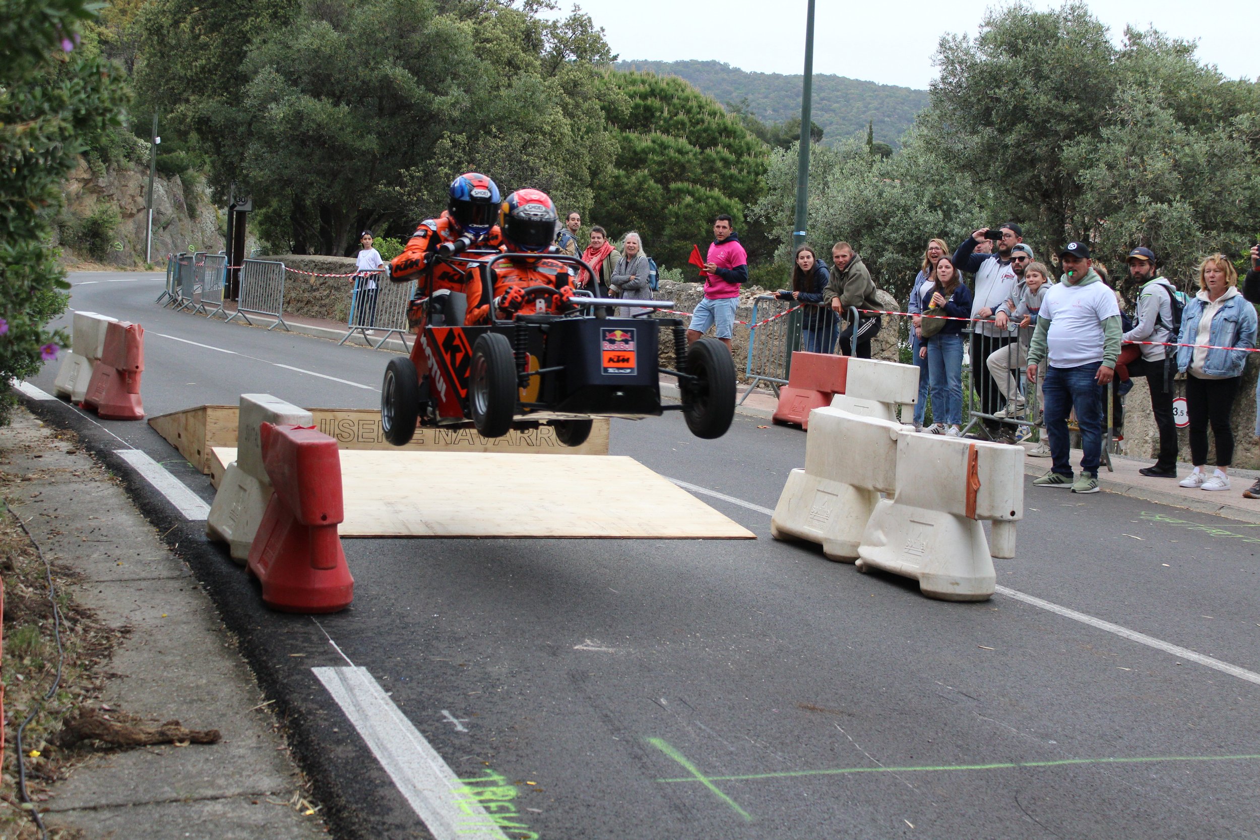 Une voiture de course, un quadricycle, en plein saut lors d'une course de rallye, avec des spectateurs qui regardent derrière des barrières.