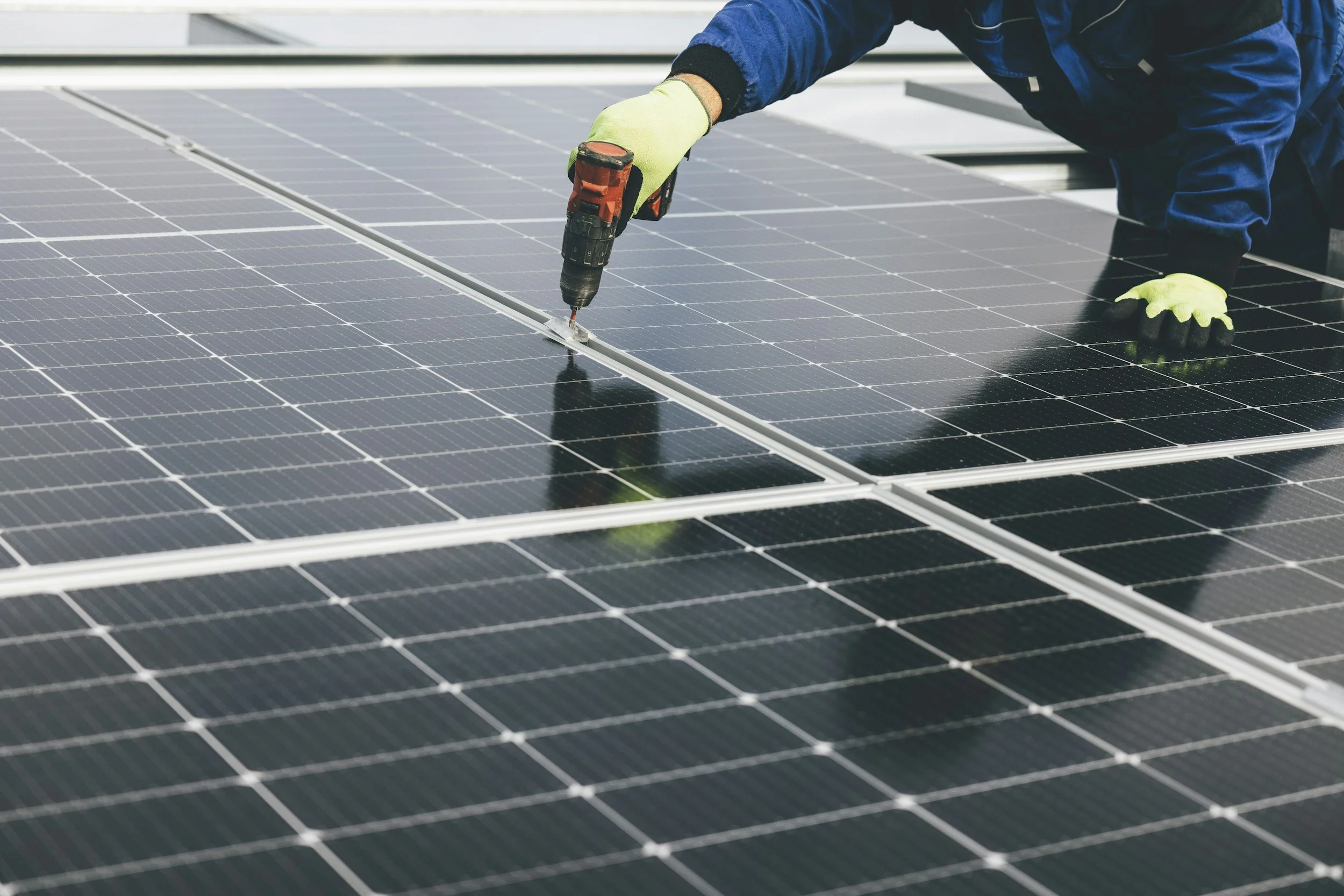 A person installing or maintaining solar panels, using a cordless drill on a rooftop with multiple solar panels.