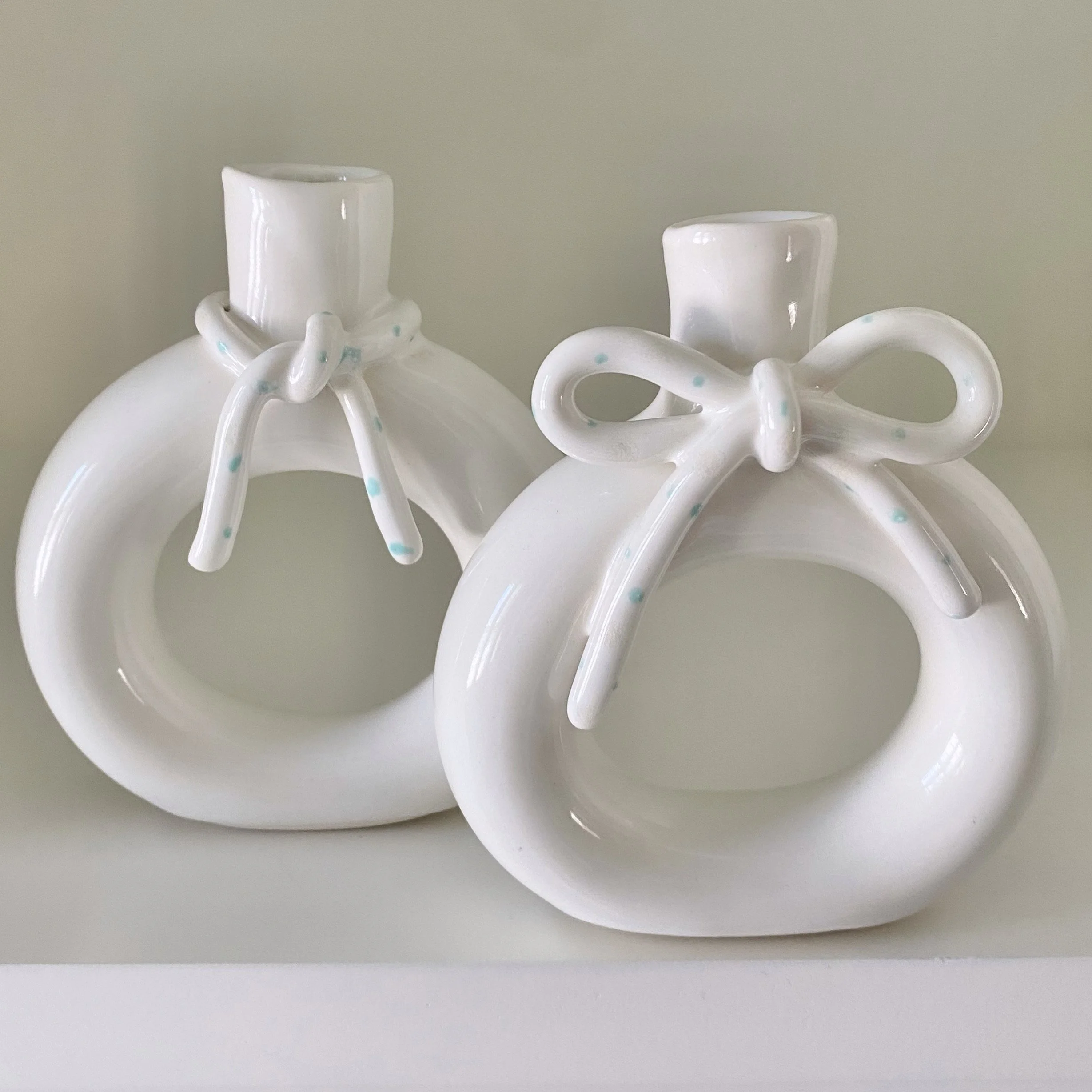 Two white ceramic vases with bow decorations on the necks, placed side by side on a white surface.