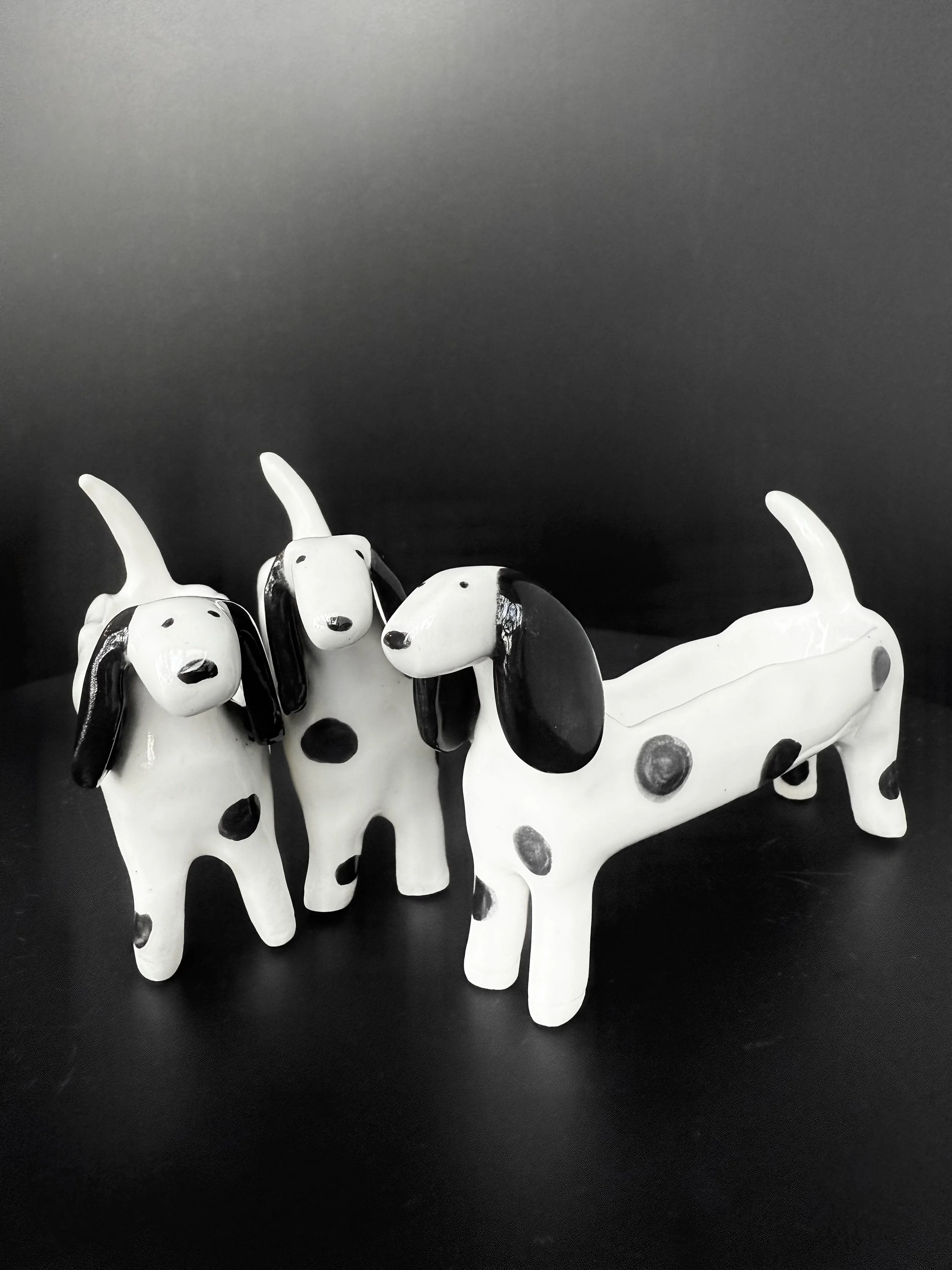 Three ceramic dog figurines with black and white spots on a black background