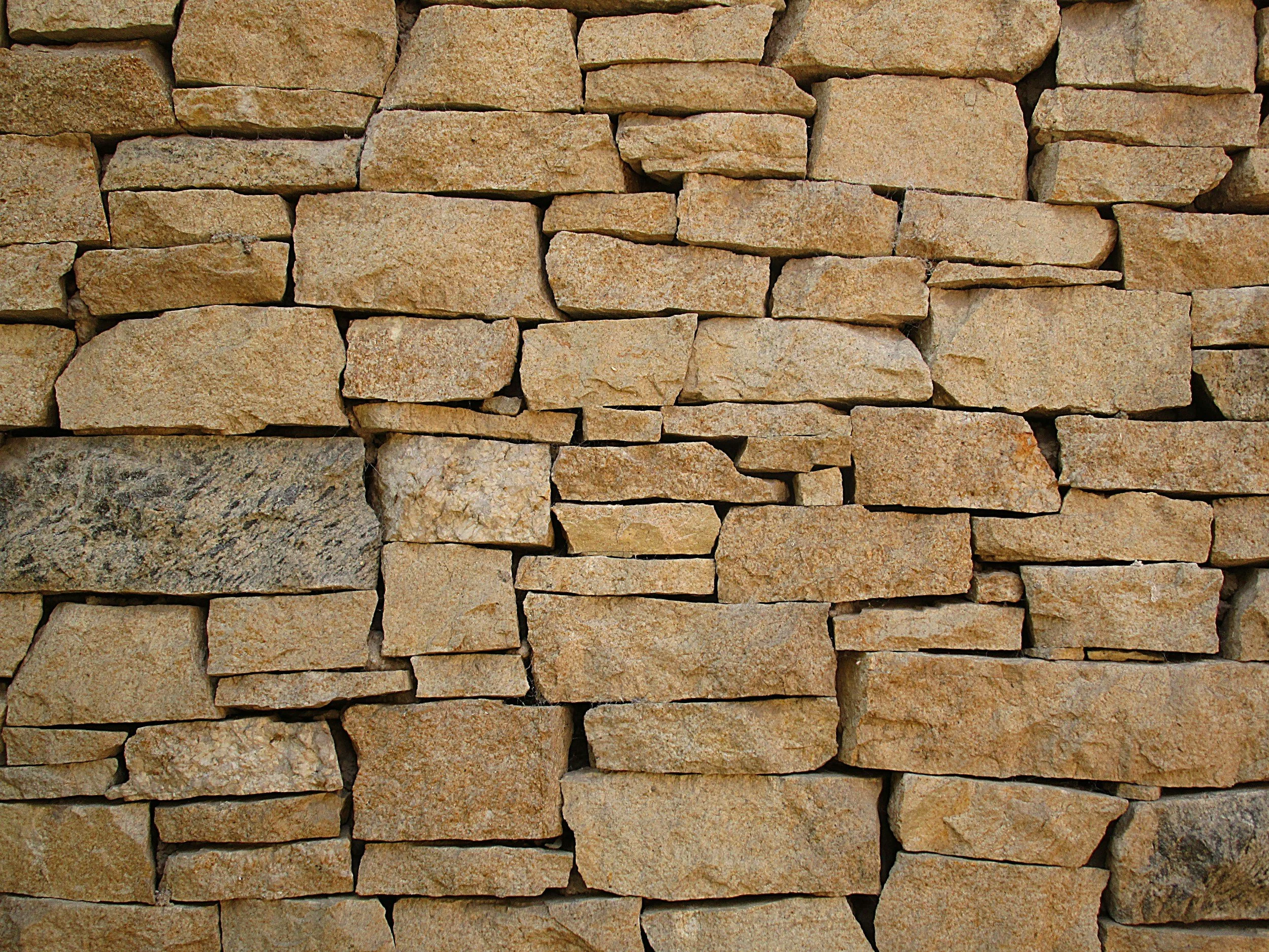 Close-up of a dry stone wall made of variously sized and shaped stacked tan and beige stones.