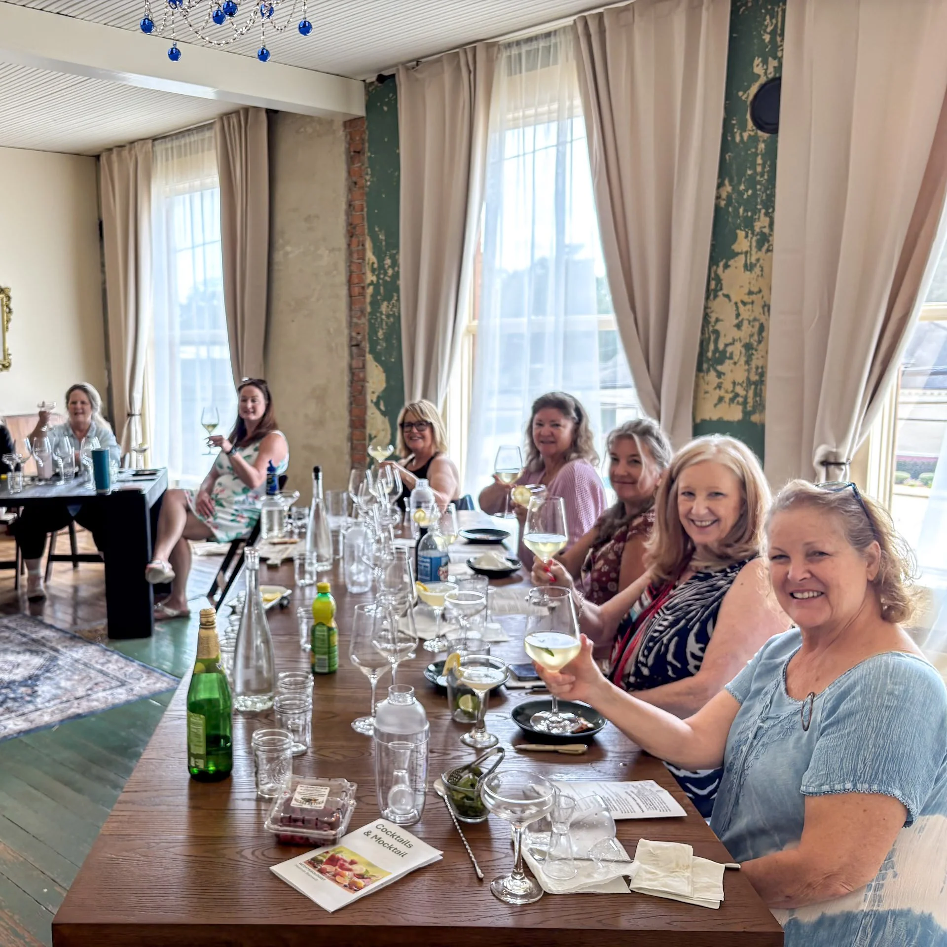 Close-up of a white magnolia flower blooming on a tree with dark green leaves, with a blurred background of a sunny outdoor setting.