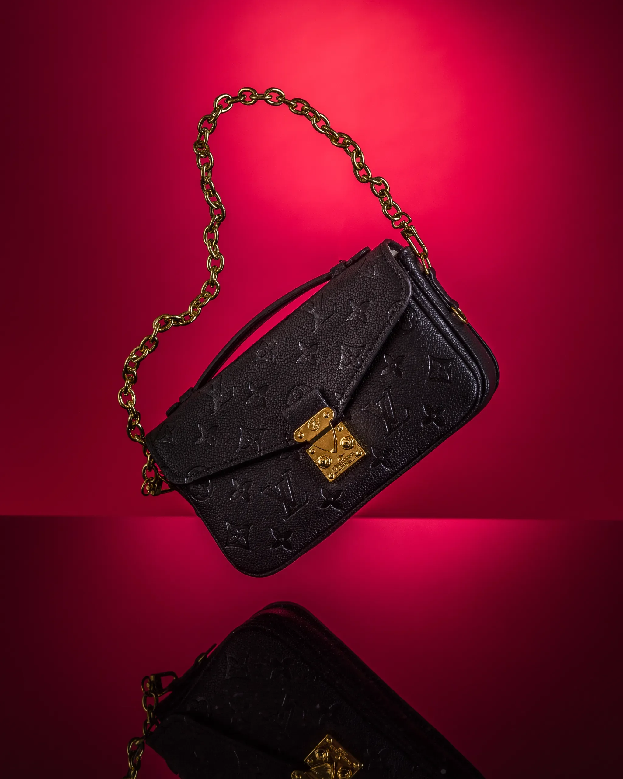 commercial product photography studio image of a black designer handbag with a gold chain strap and gold hardware, resting against a red background