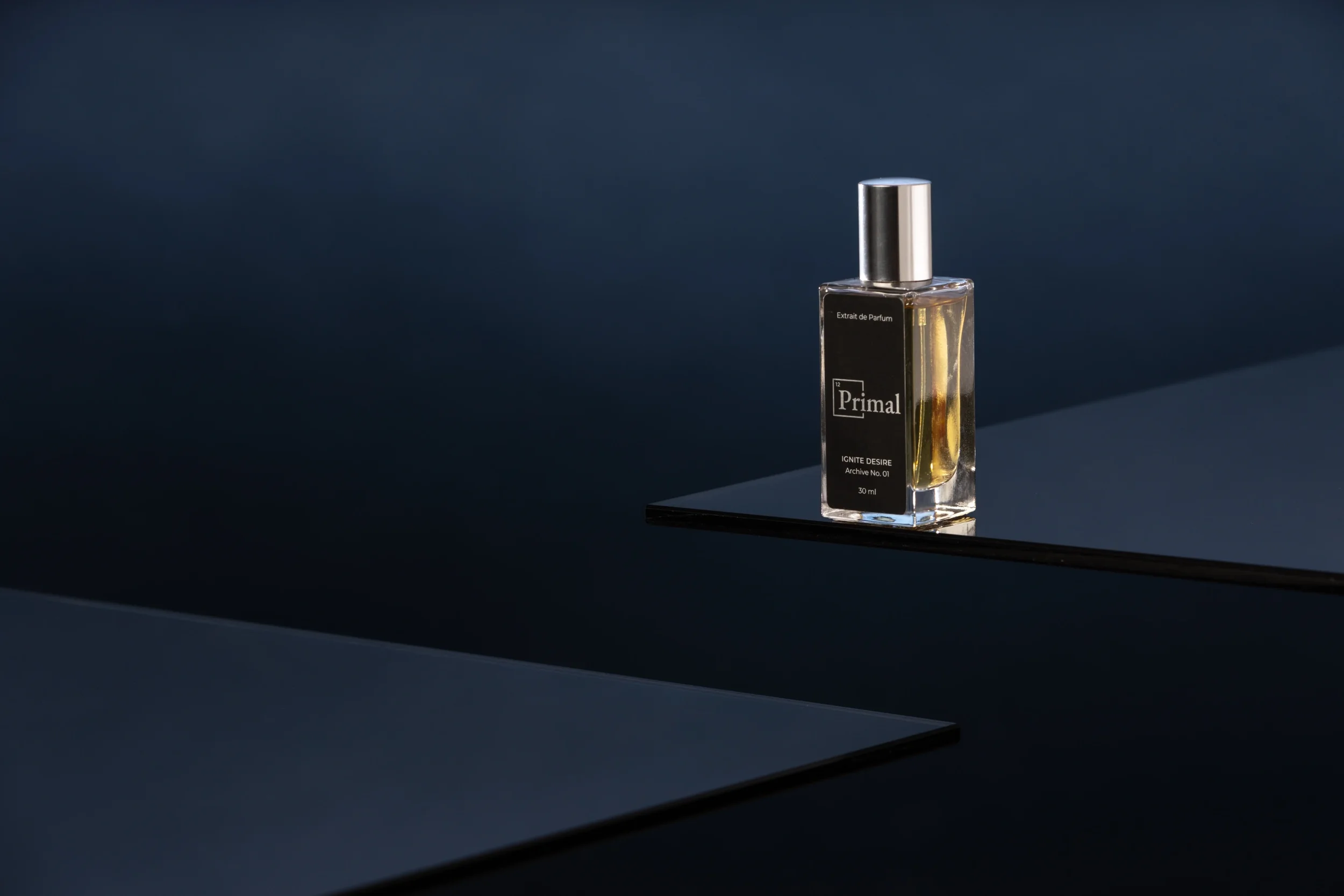 commercial product photography studio image of a clear glass perfume bottle with a silver cap stands on a dark surface, with a dark background.