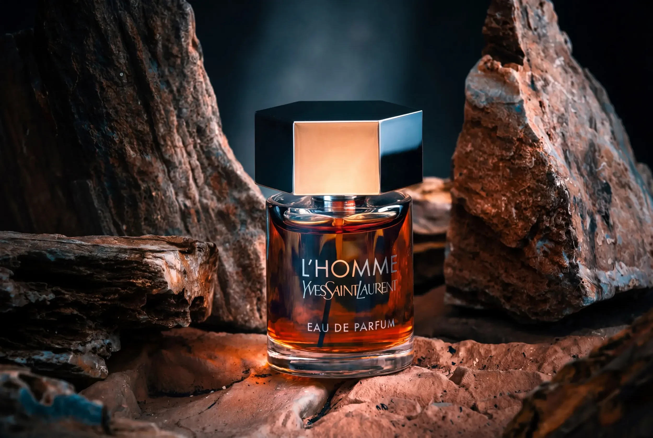 Lifestyle photograph of a bottle of Yves Saint Laurent L'Homme Eau de Parfum nestled among rocks with a dark background, taken in a commercial product photography studio