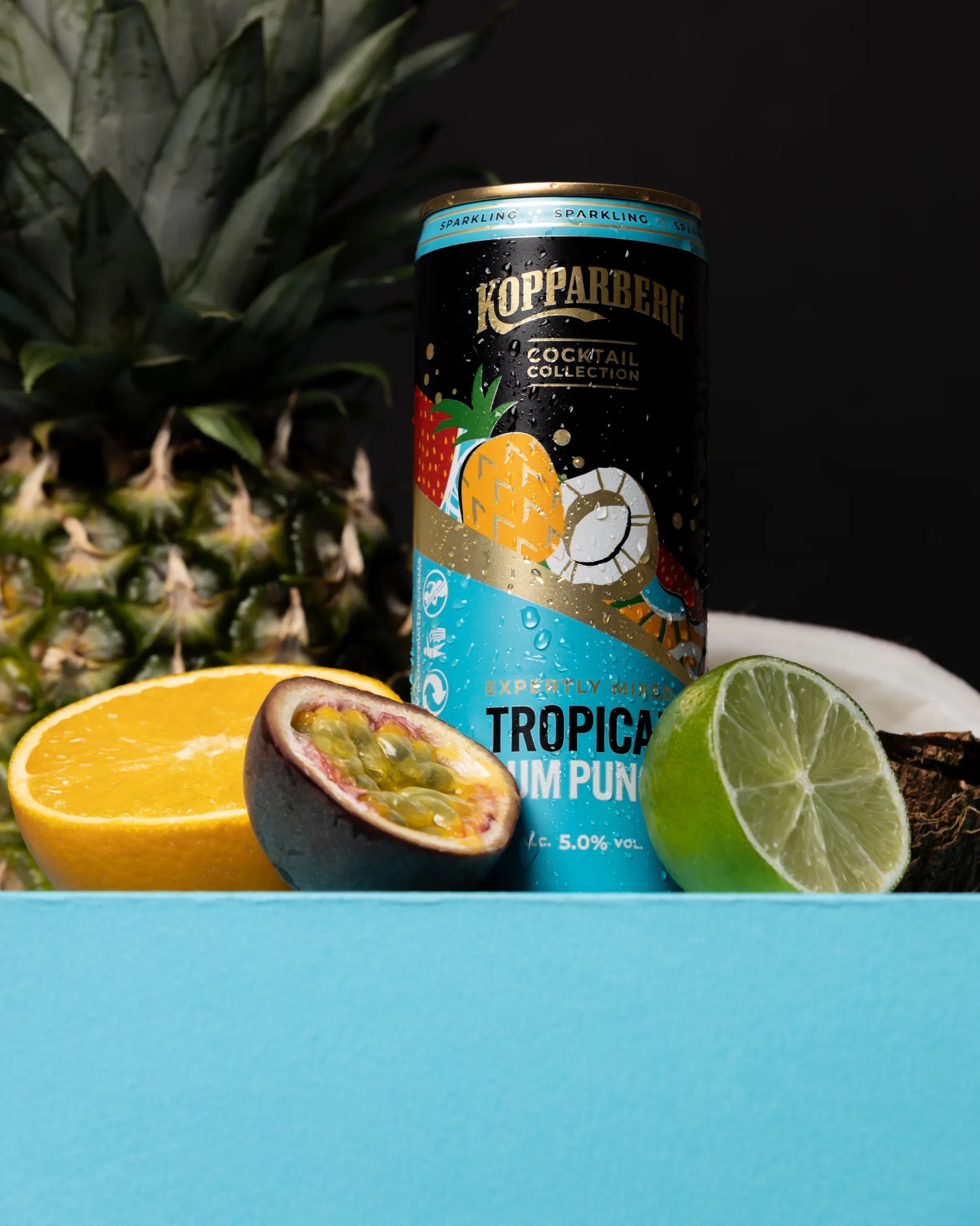 commercial product photography studio image of a can of Kopparberg Tropical Fruit Punch and tropical fruits including lemon, lime, passion fruit, pineapple, and a coconut