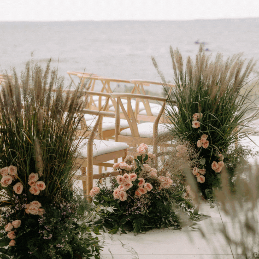 Empty chairs and floral arrangements on a beach deck facing the ocean.
